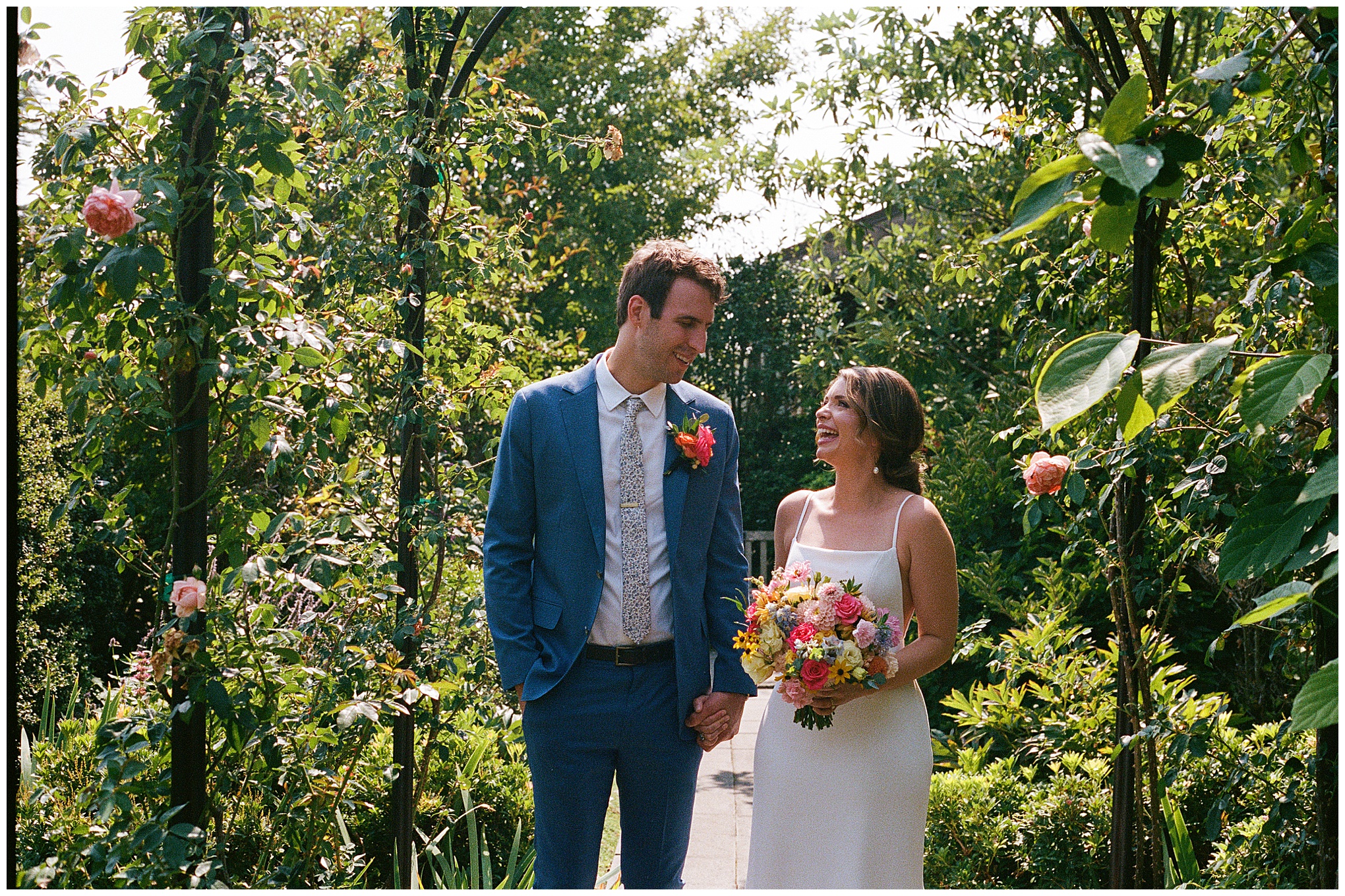 Bride and groom smiling and holding hands in the garden.