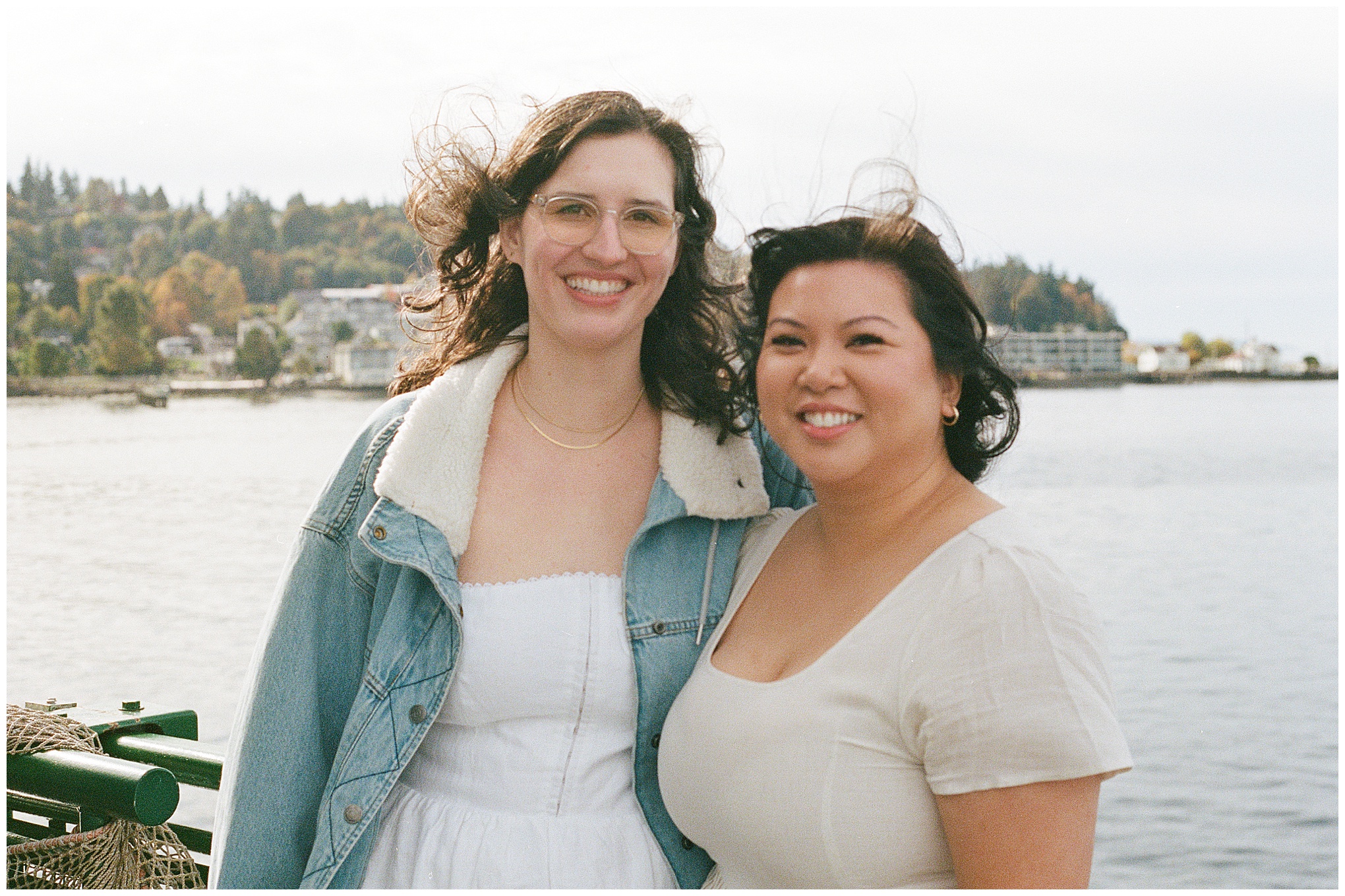 Carli and Erin smiling together with the Whidbey Island shore in the background.