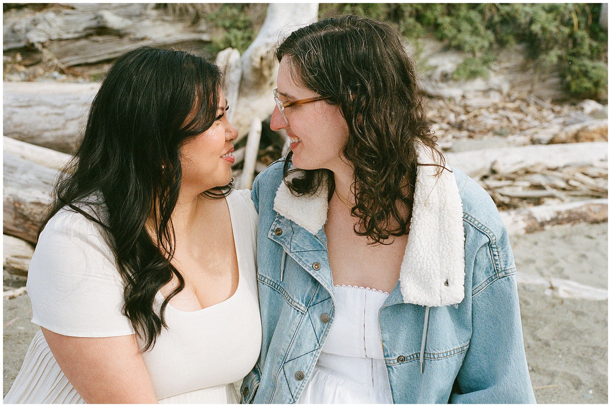 Carli and Erin sitting close and smiling at each other on the beach.