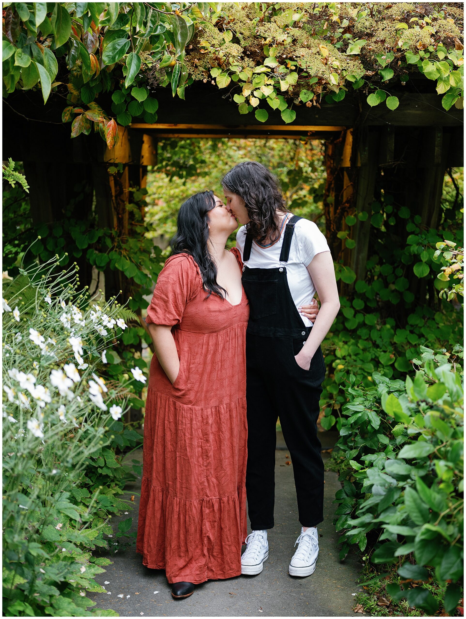 Carli and Erin kissing under a lush, leafy archway.