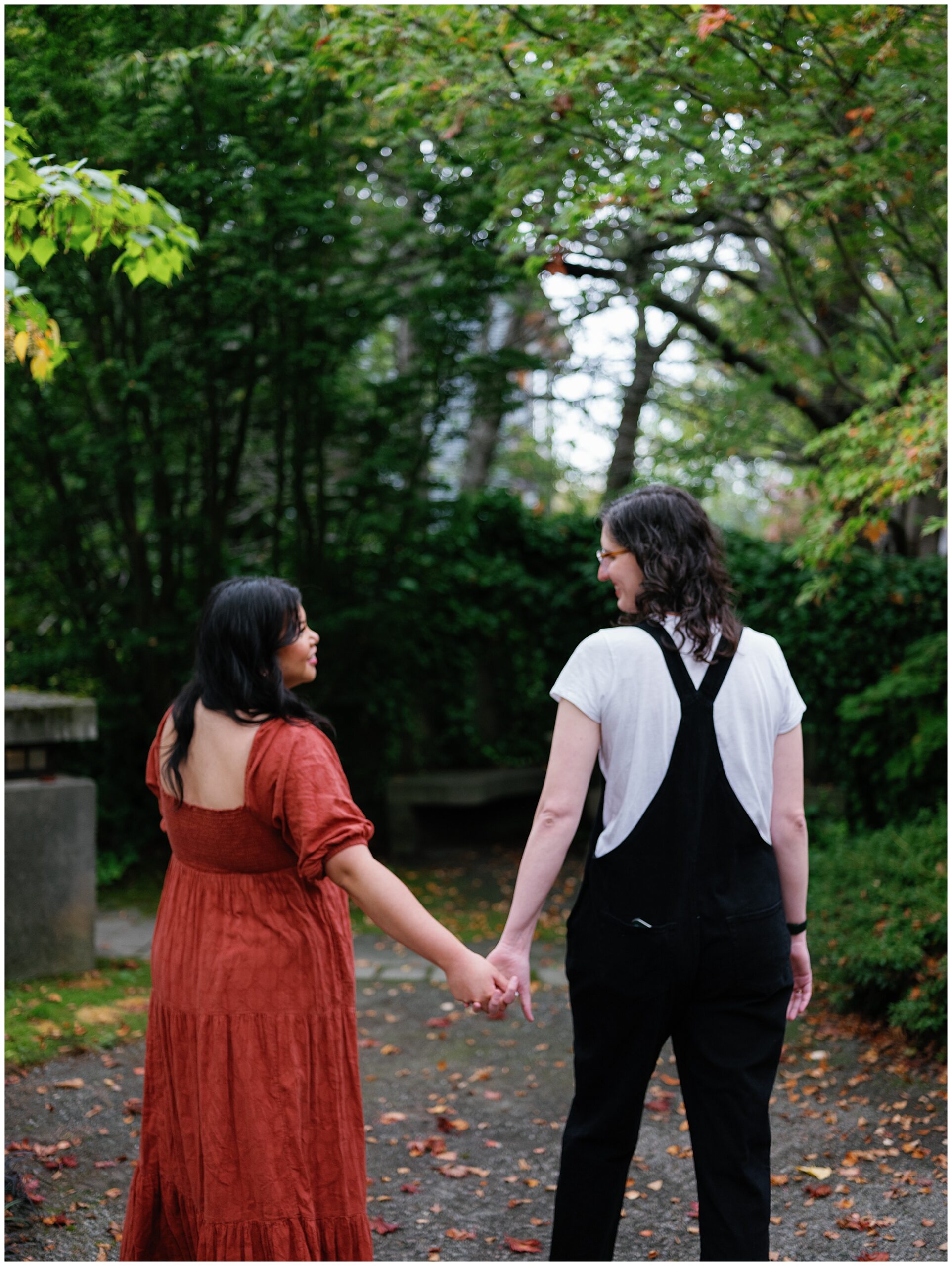 Carli and Erin walking hand in hand through a leafy path.