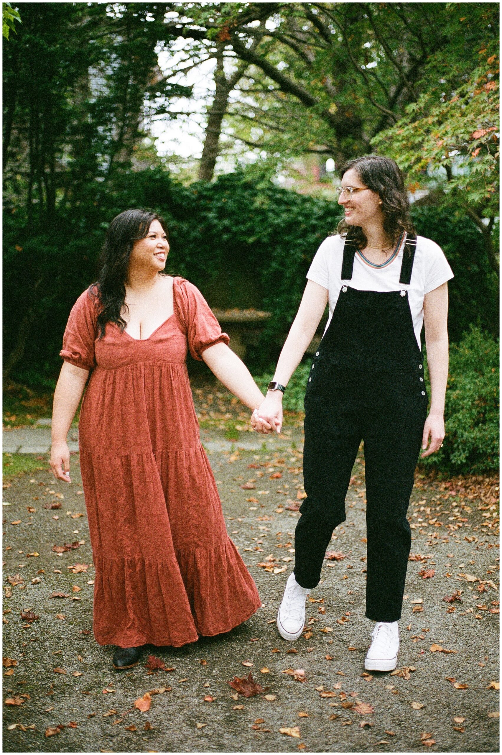 Carli and Erin hold hands and walk through a leafy garden path.