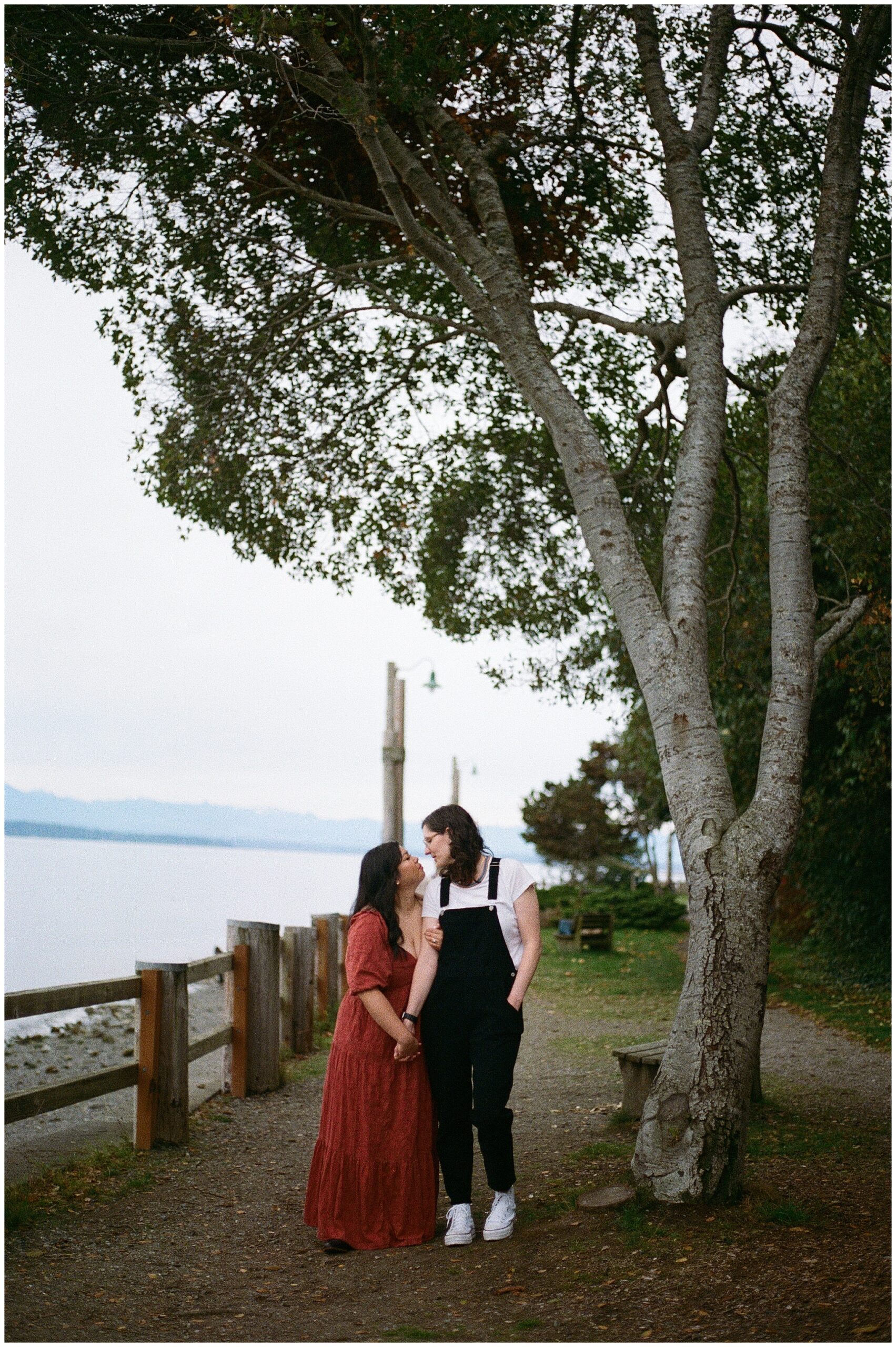 Carli and Erin walk hand-in-hand through a garden, looking at each other lovingly.