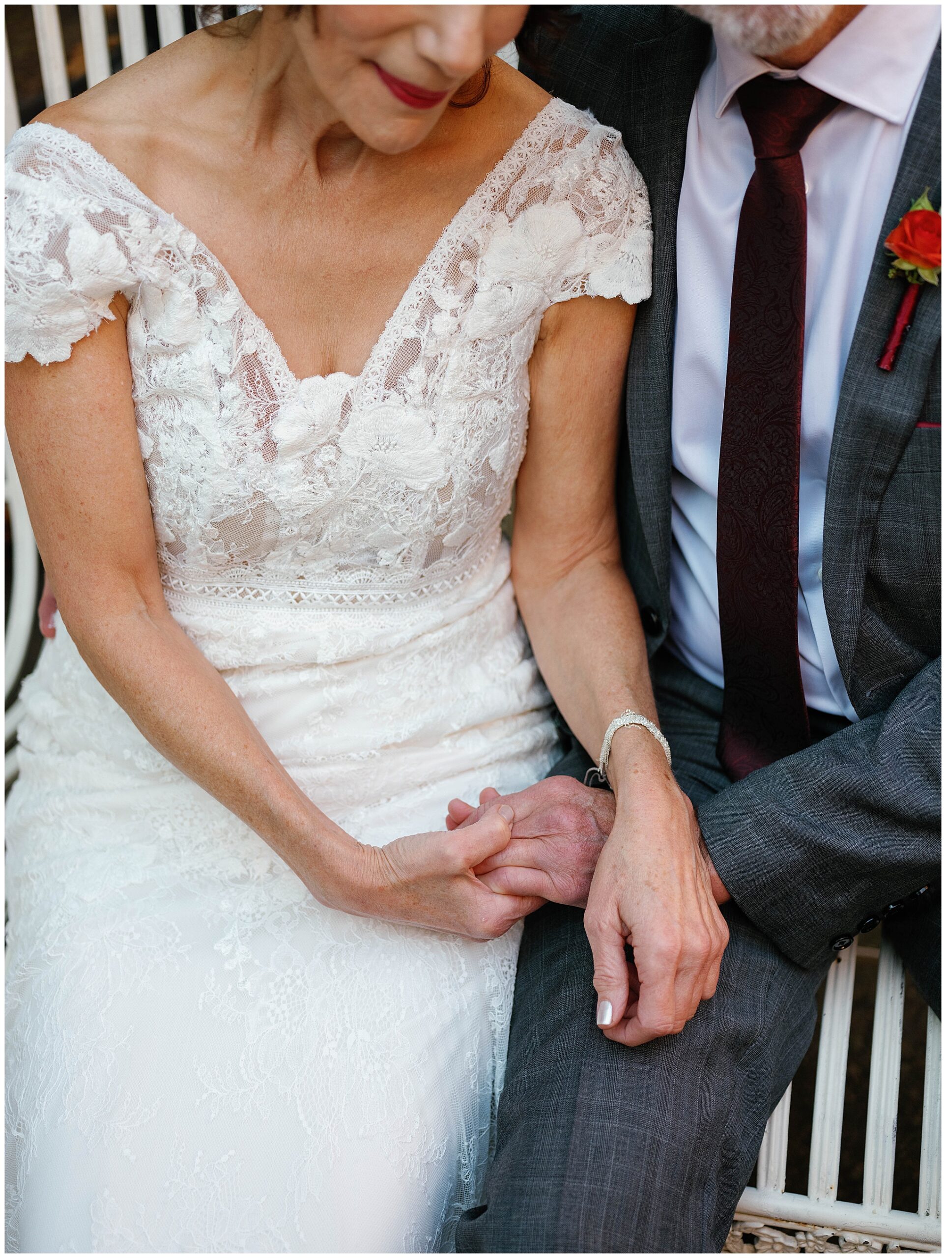 Bride and groom seated, holding hands, intimate moment.