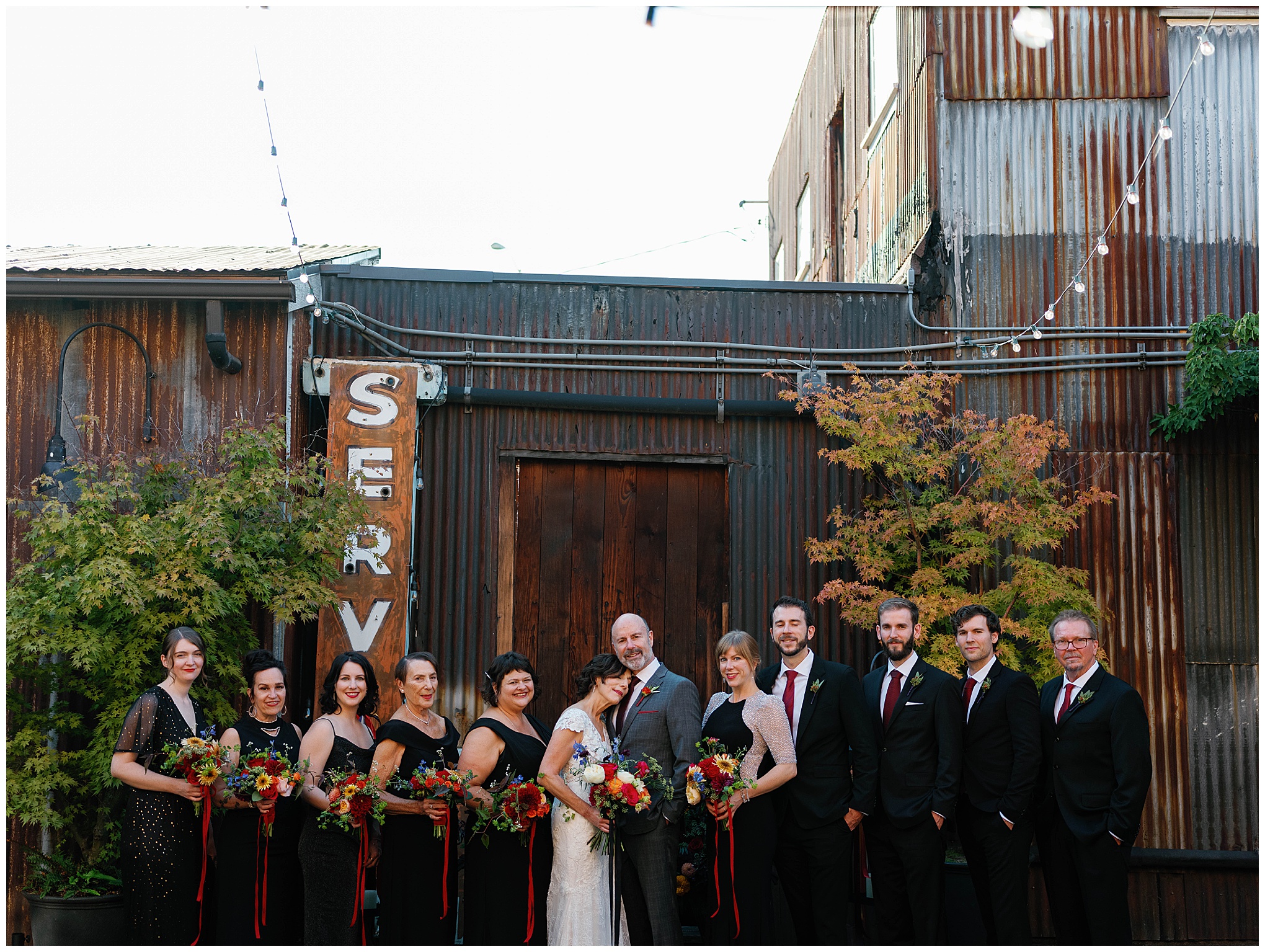 Wedding party group photo in front of rustic building.