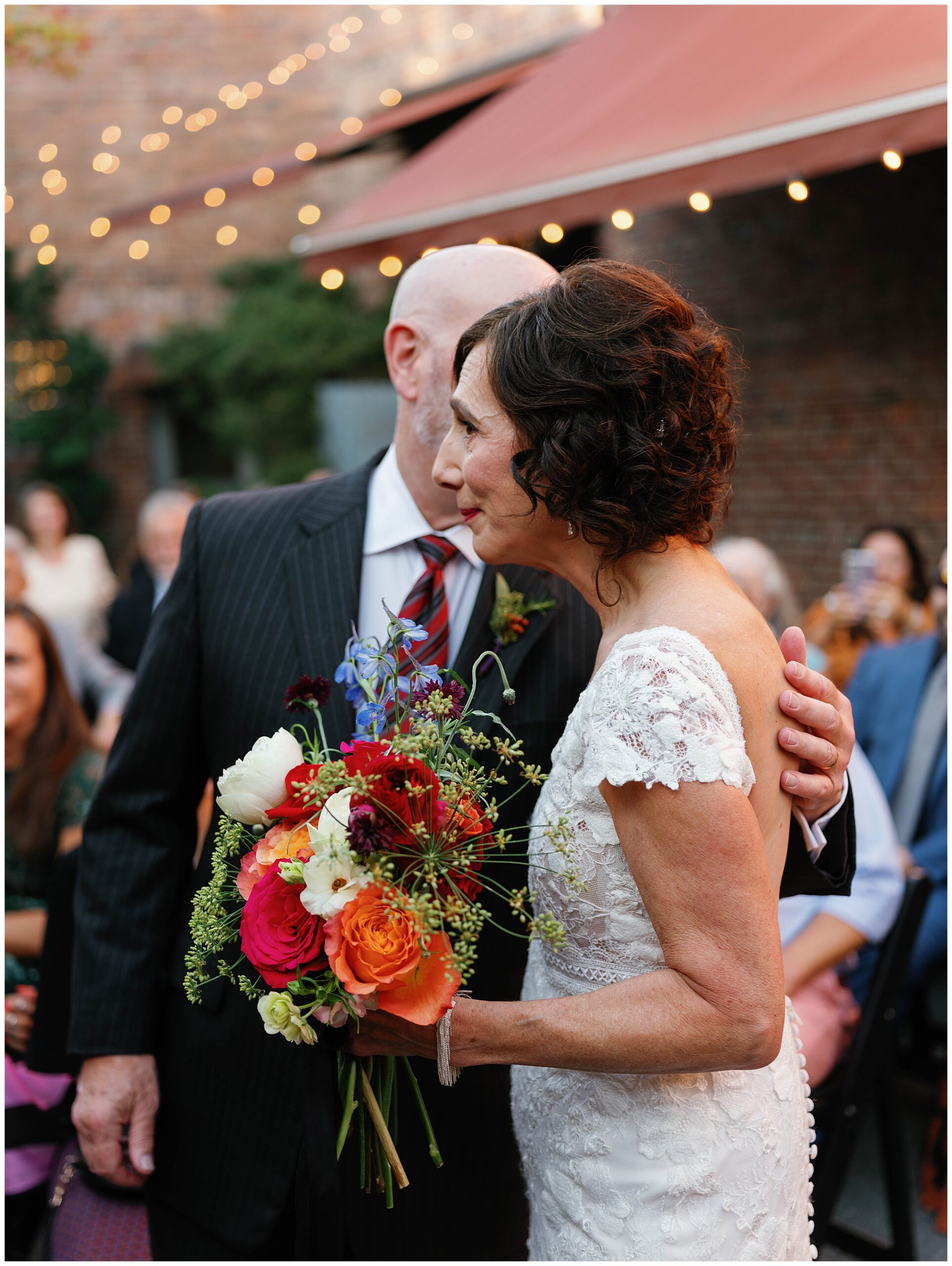 Bride holding vibrant bouquet as she embraces a loved one during the ceremony.