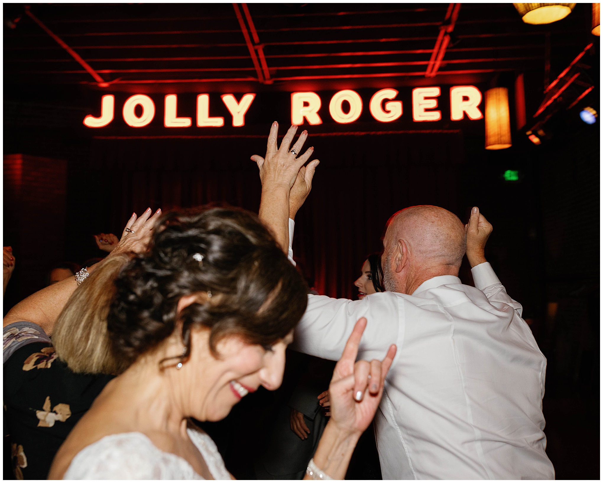 Wedding guests dancing enthusiastically under the Jolly Roger sign.