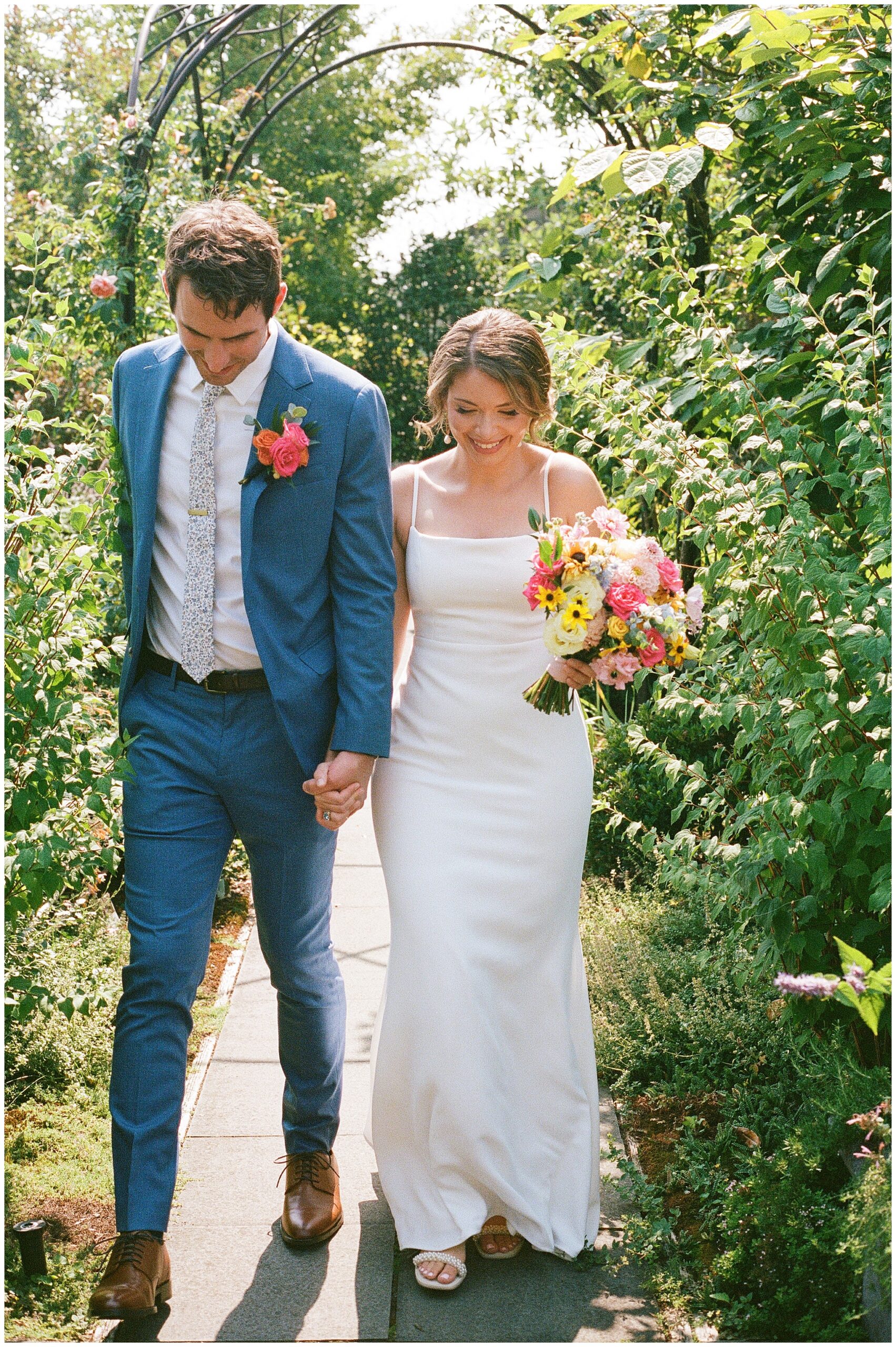 Couple walking hand in hand down a garden path.