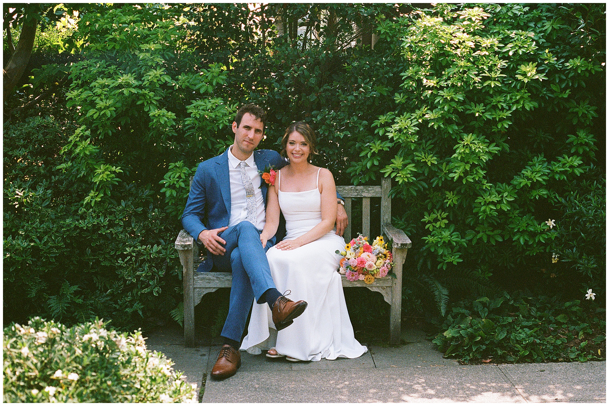 Bride and groom sit smiling beside each other on a bench