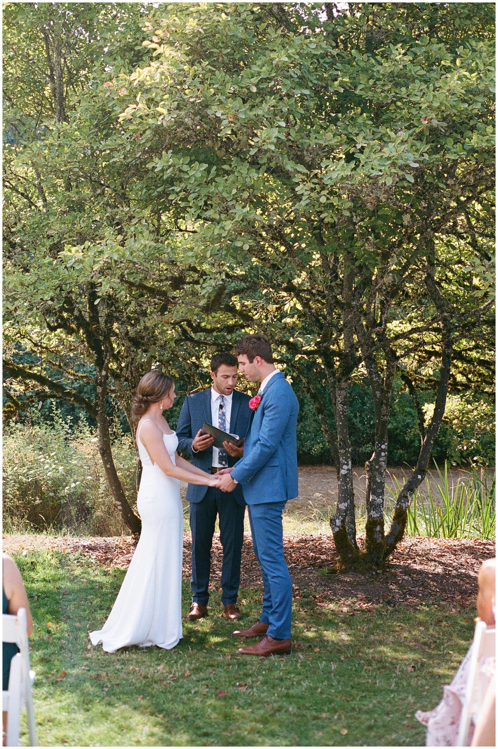 Grace and Chris hold hands and exchange vows under a canopy of trees at the Center for Urban Horticulture.