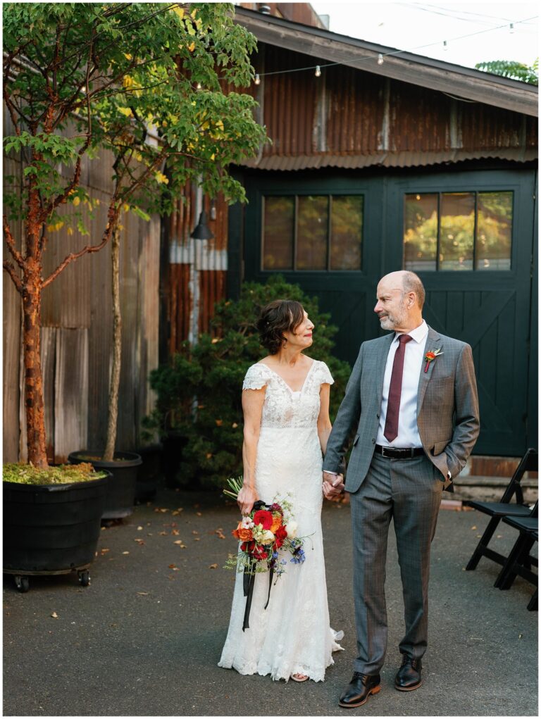 Bride and groom walking hand in hand, smiling at each other.