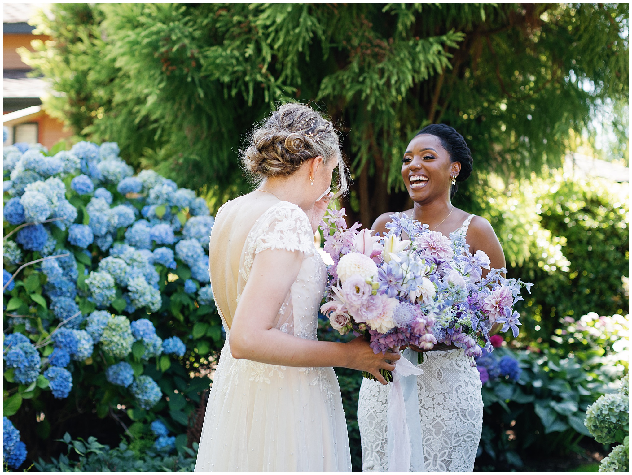 Brides sharing a laugh amidst blue hydrangeas during their first look.