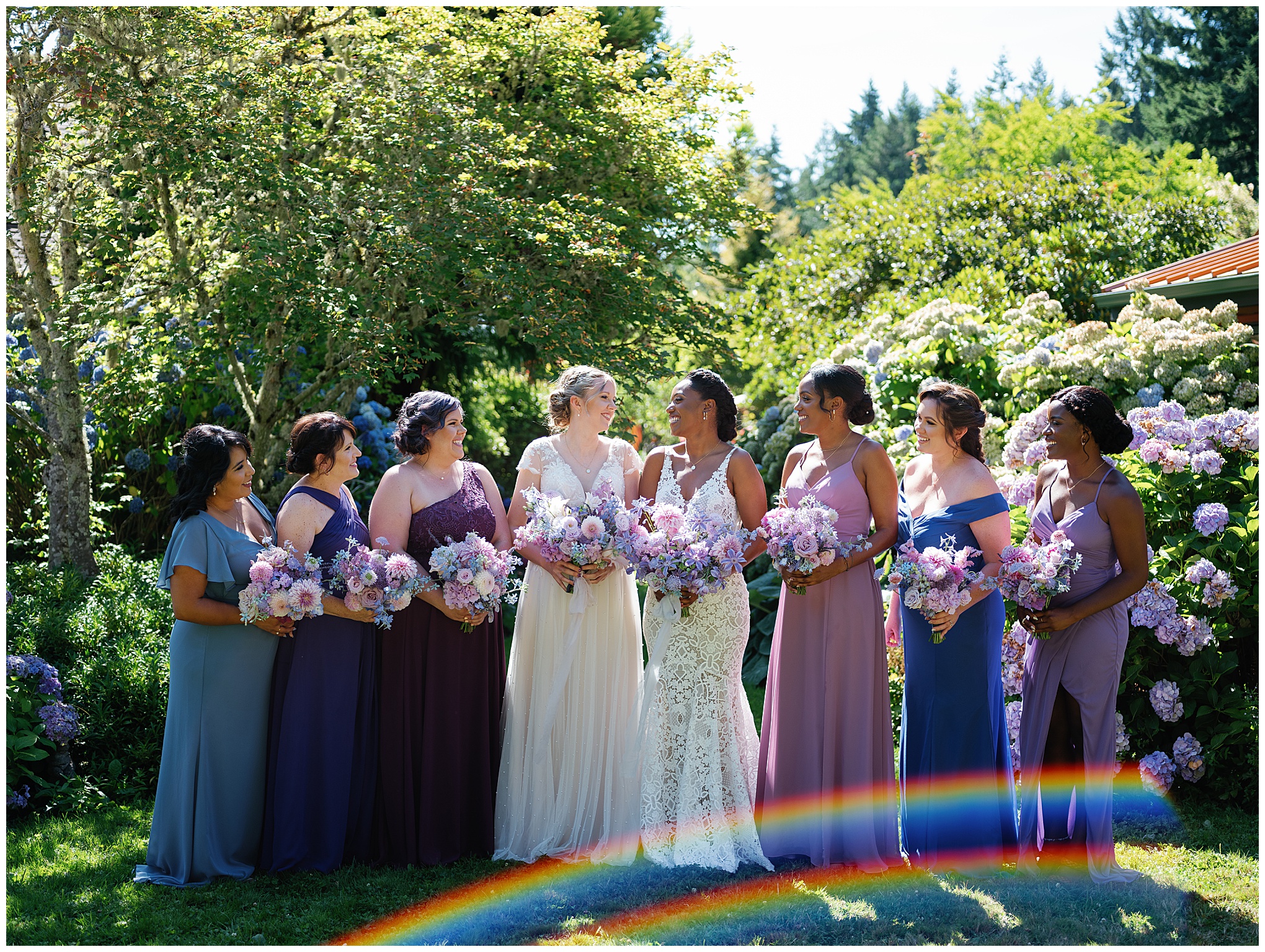 Bridesmaids in varying shades of purple and blue dresses, standing with the brides, holding matching bouquets of purple and pink flowers.