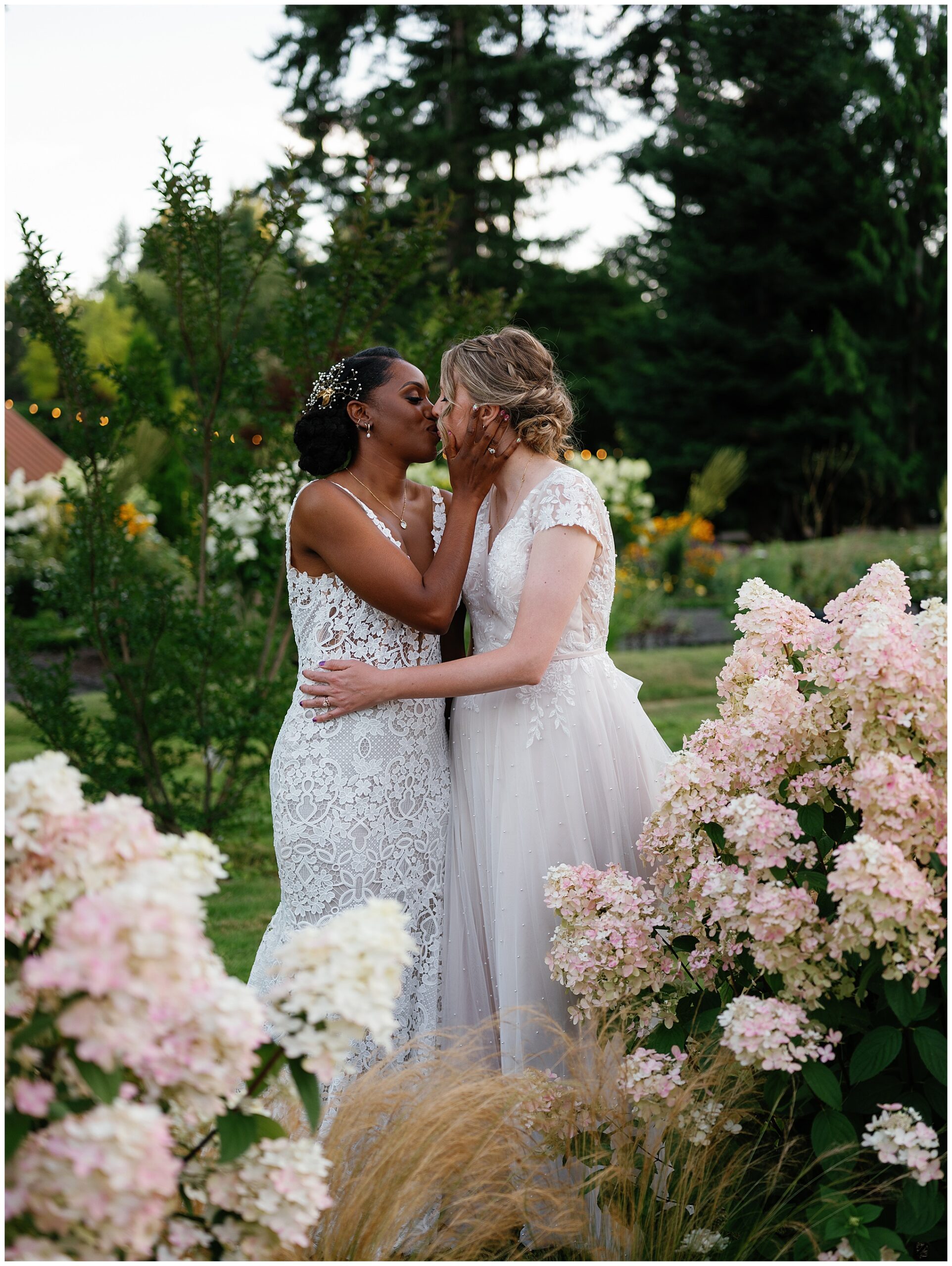 Brides share a kiss amidst hydrangeas.