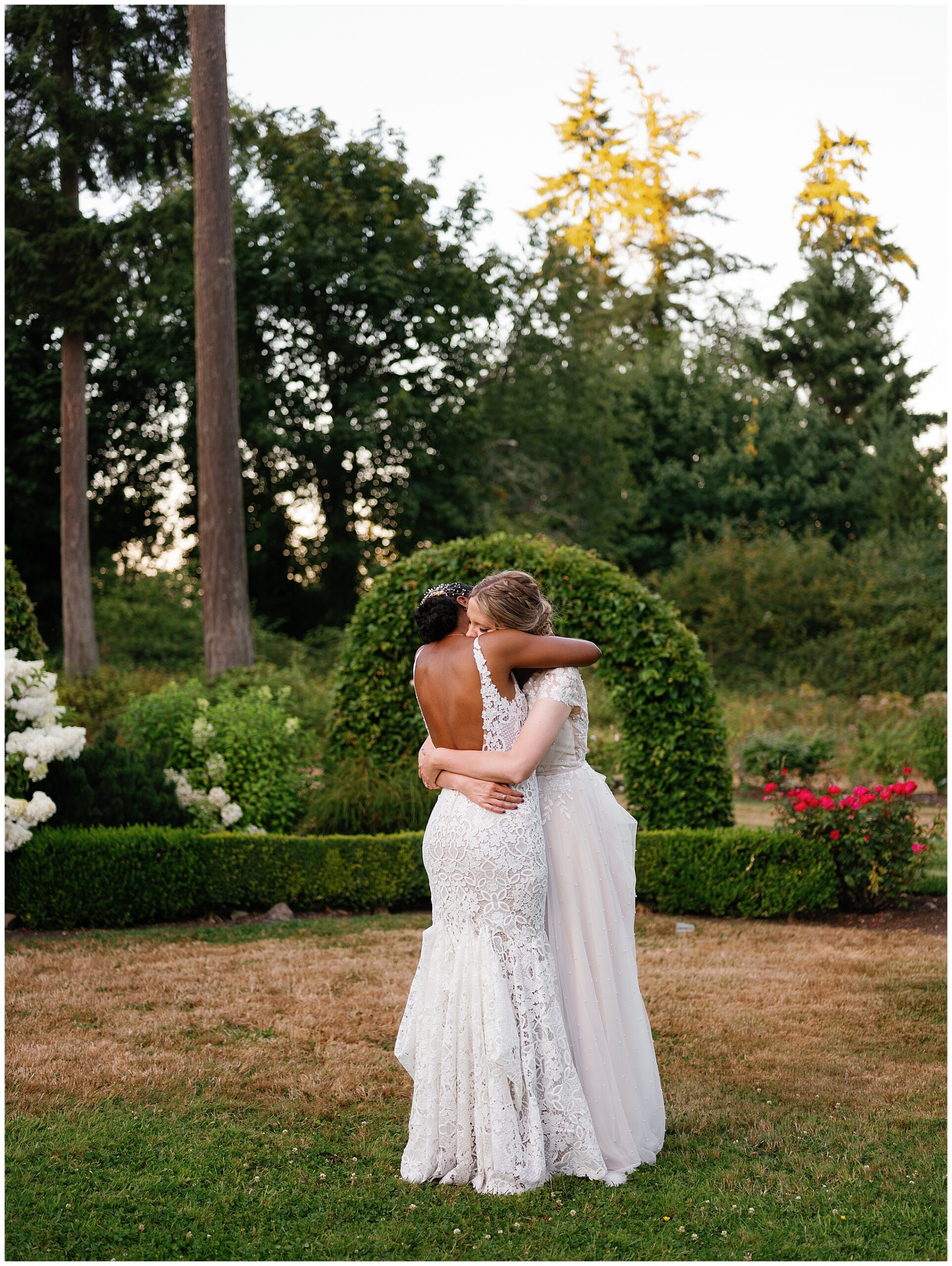 Brides hugging in front of a floral arch.