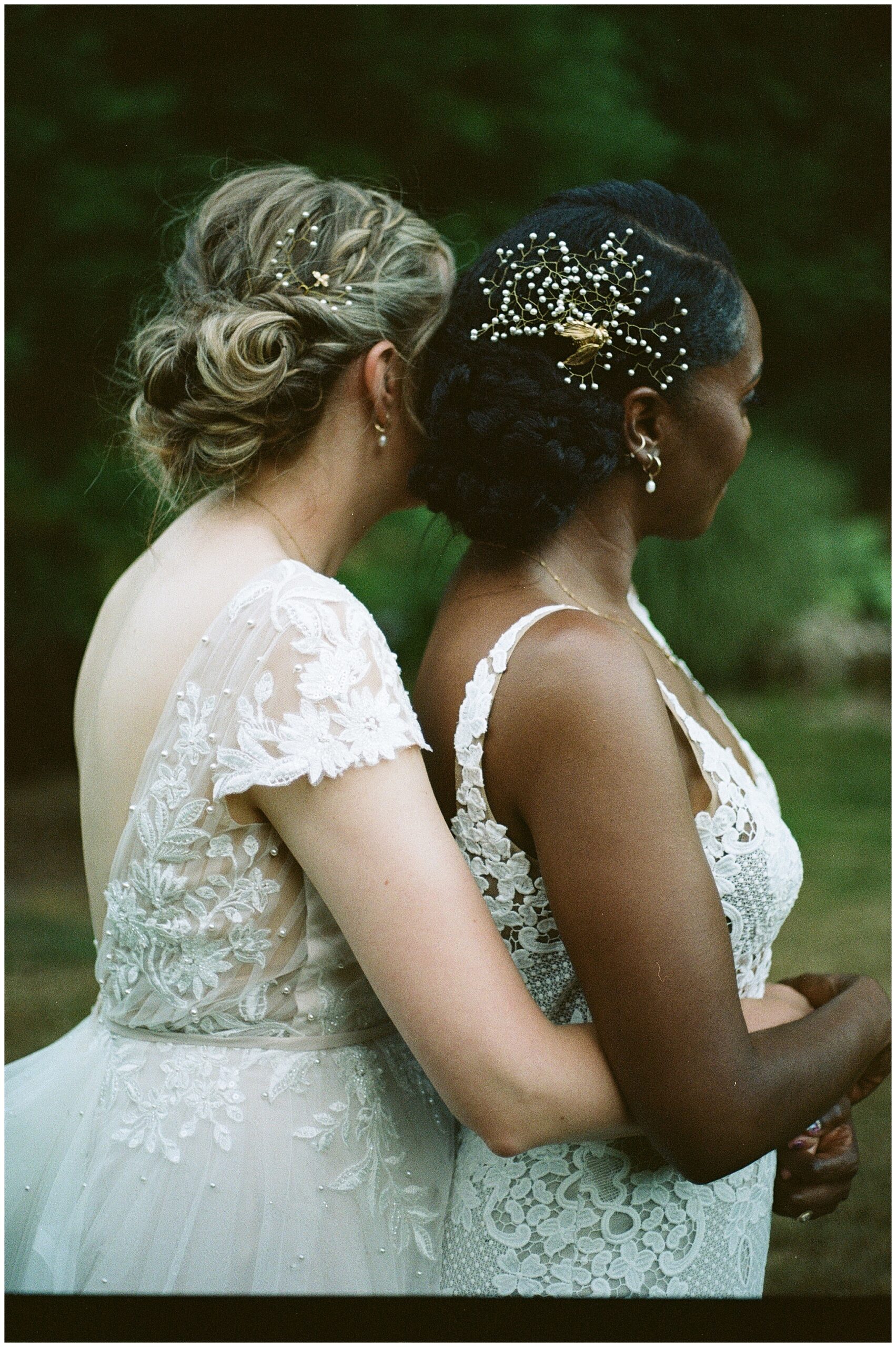 The couple stands closely, one whispering into the other's ear, adorned with intricate hair accessories.