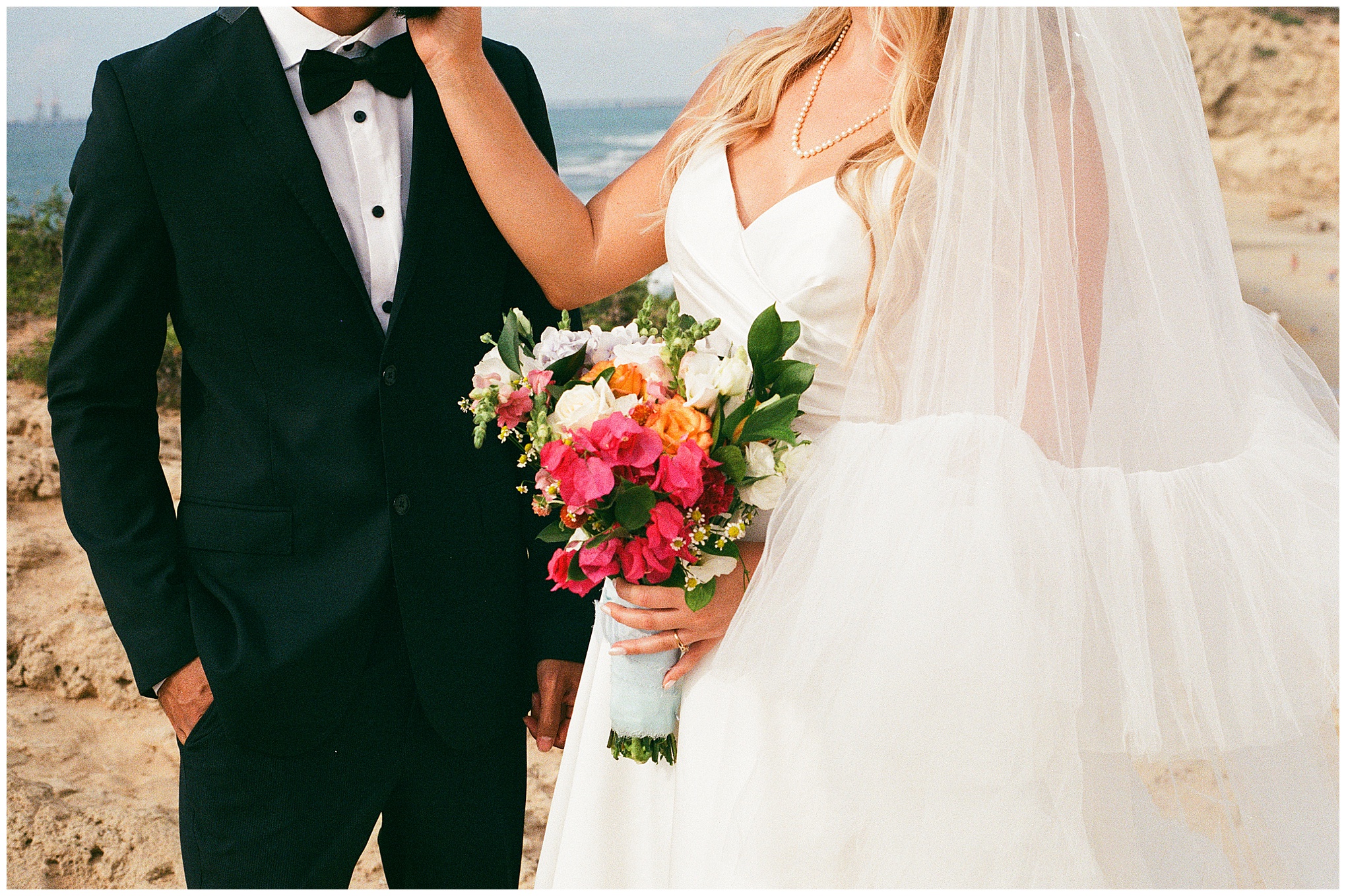 Close-up of bride holding a vibrant bouquet of pink, white, and orange flowers, standing beside the groom in a dark suit.