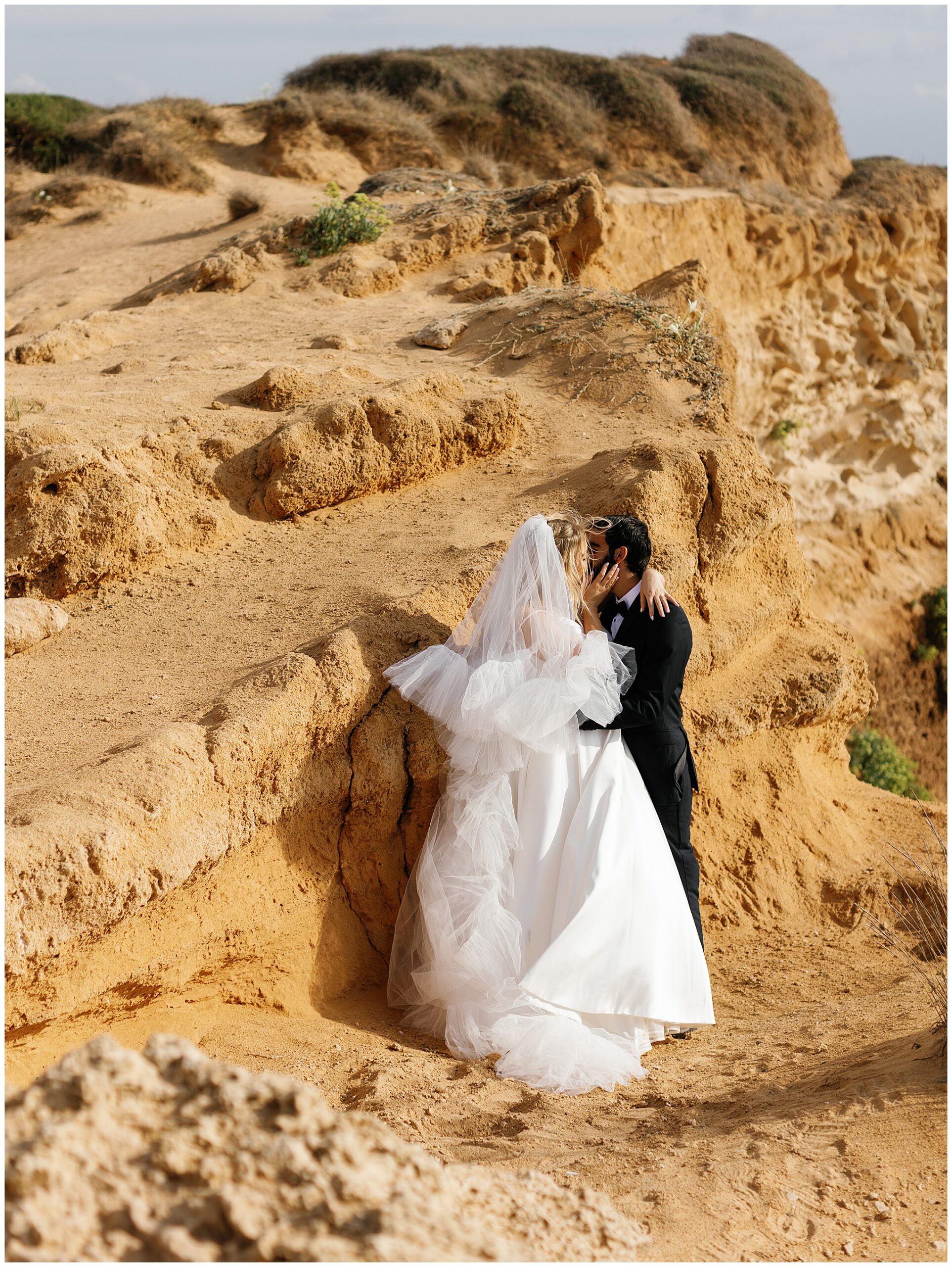 Bride and groom share a kiss nestled against a rocky cliff during their Mediterranean wedding.