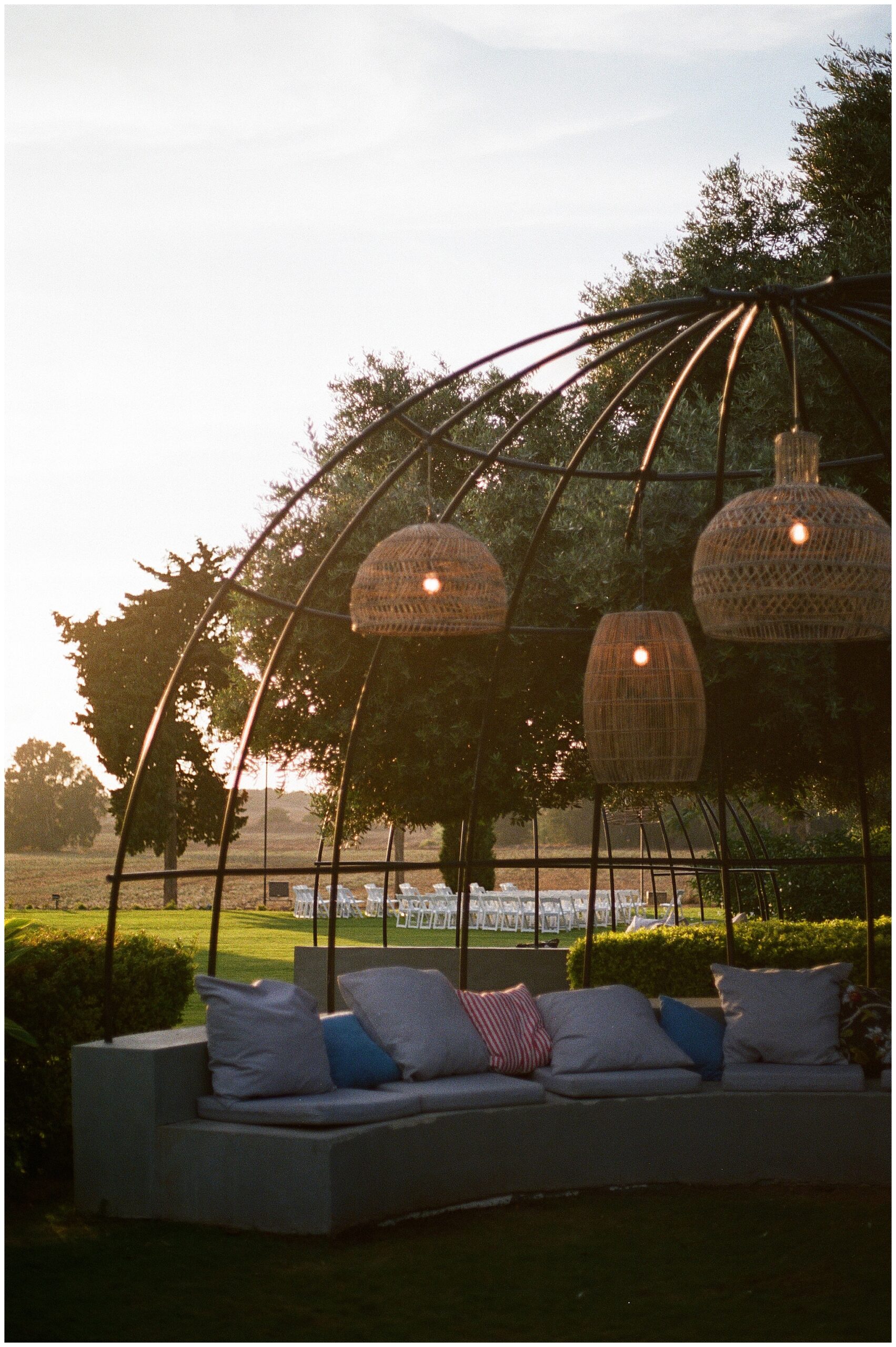 Cozy outdoor lounge area with pillows and lanterns hanging overhead, set against a lush green landscape.