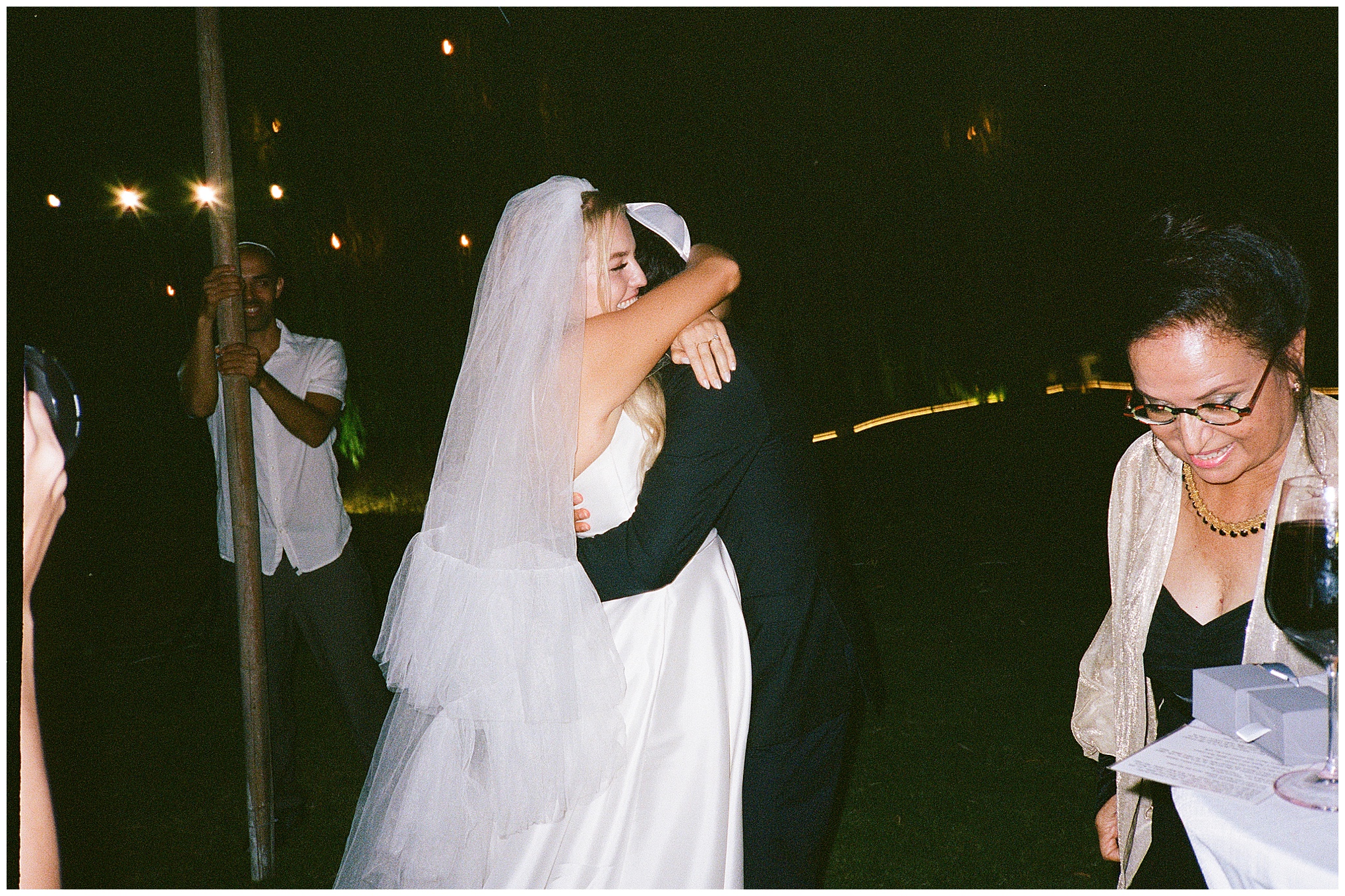 Bride and groom share an emotional hug after the ceremony, surrounded by loved ones during their evening wedding celebration.