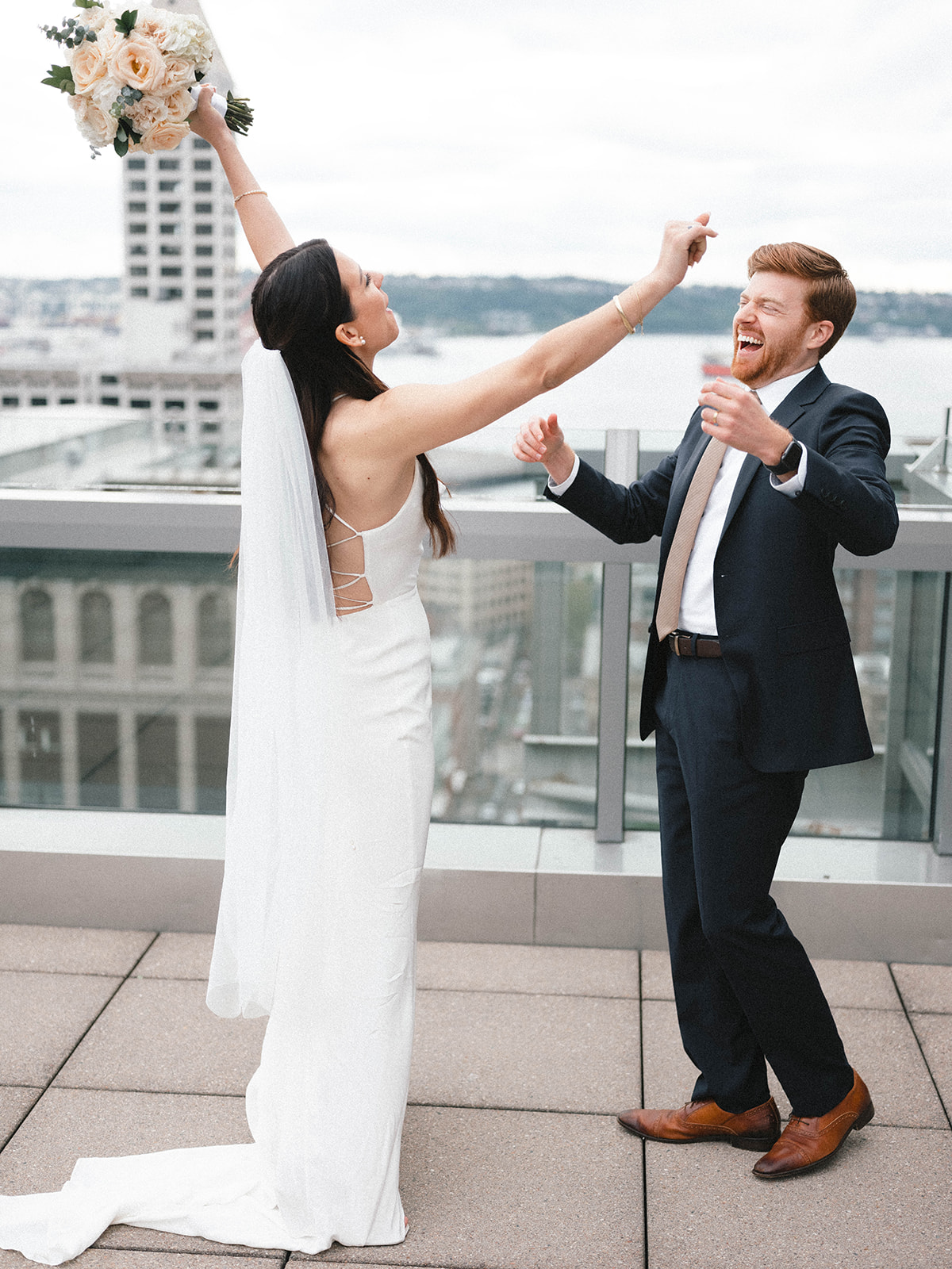 Bride raising her bouquet in celebration with the groom after their rooftop Seattle courthouse elopement.