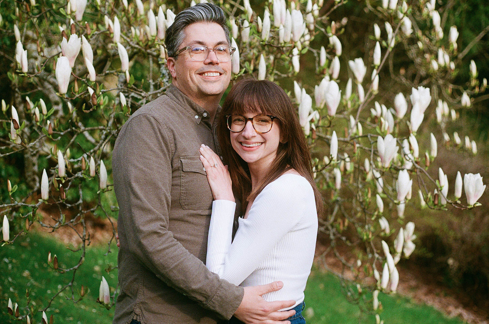 Charlotte and Grant smiling together, surrounded by blooming magnolia trees in the background.