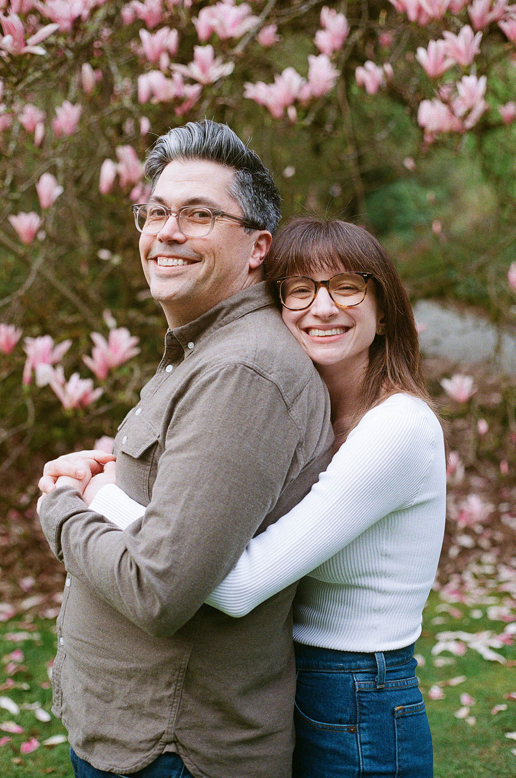 Charlotte and Grant smiling as they embrace, surrounded by magnolia trees in full bloom.