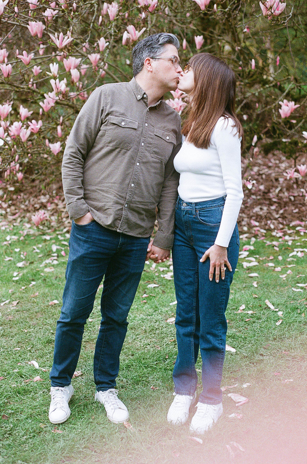 Charlotte and Grant share a kiss while holding hands in front of blooming magnolia trees at Washington Park Arboretum.