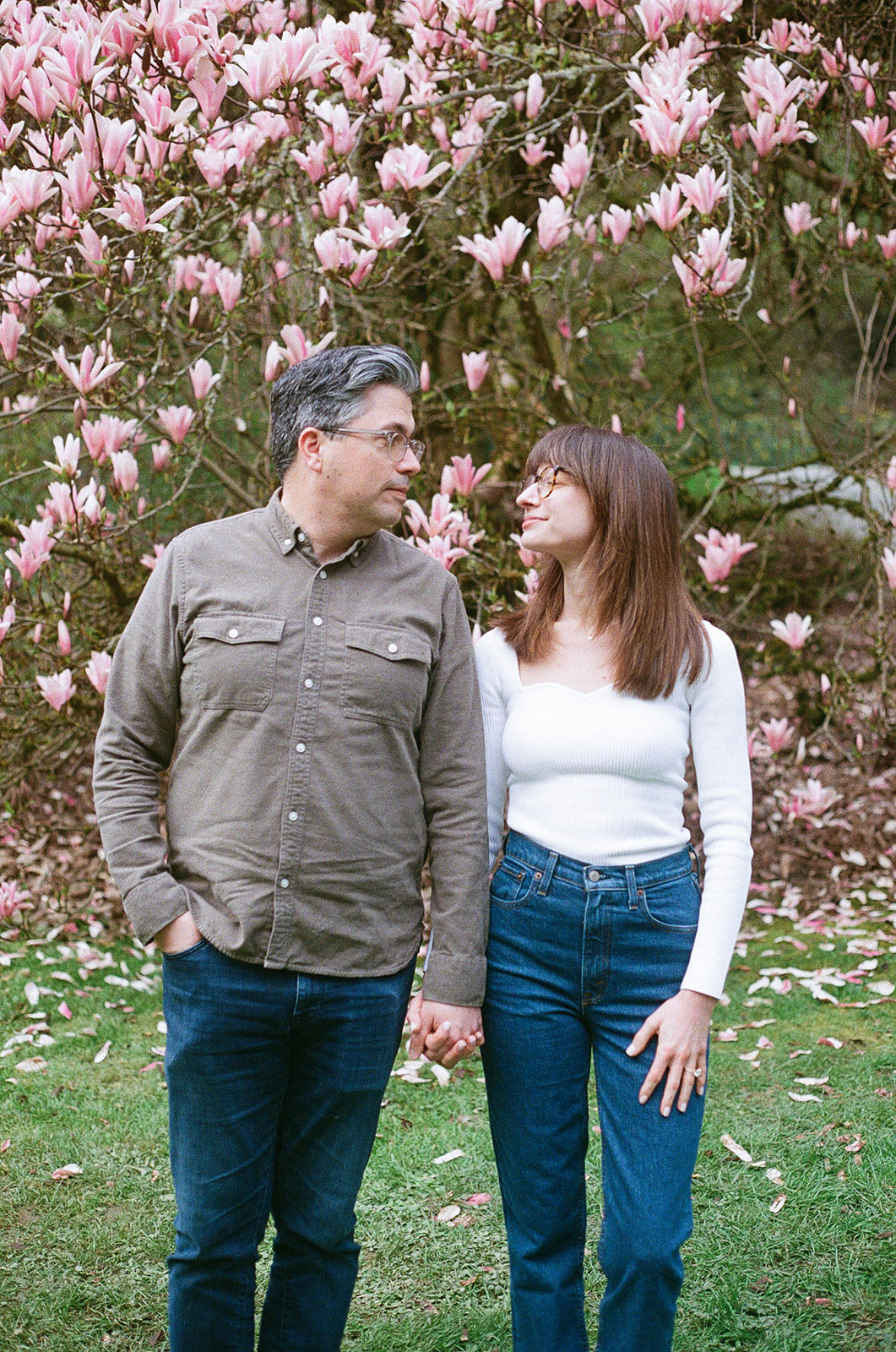 Charlotte and Grant holding hands, gazing at each other in front of a blooming magnolia tree.