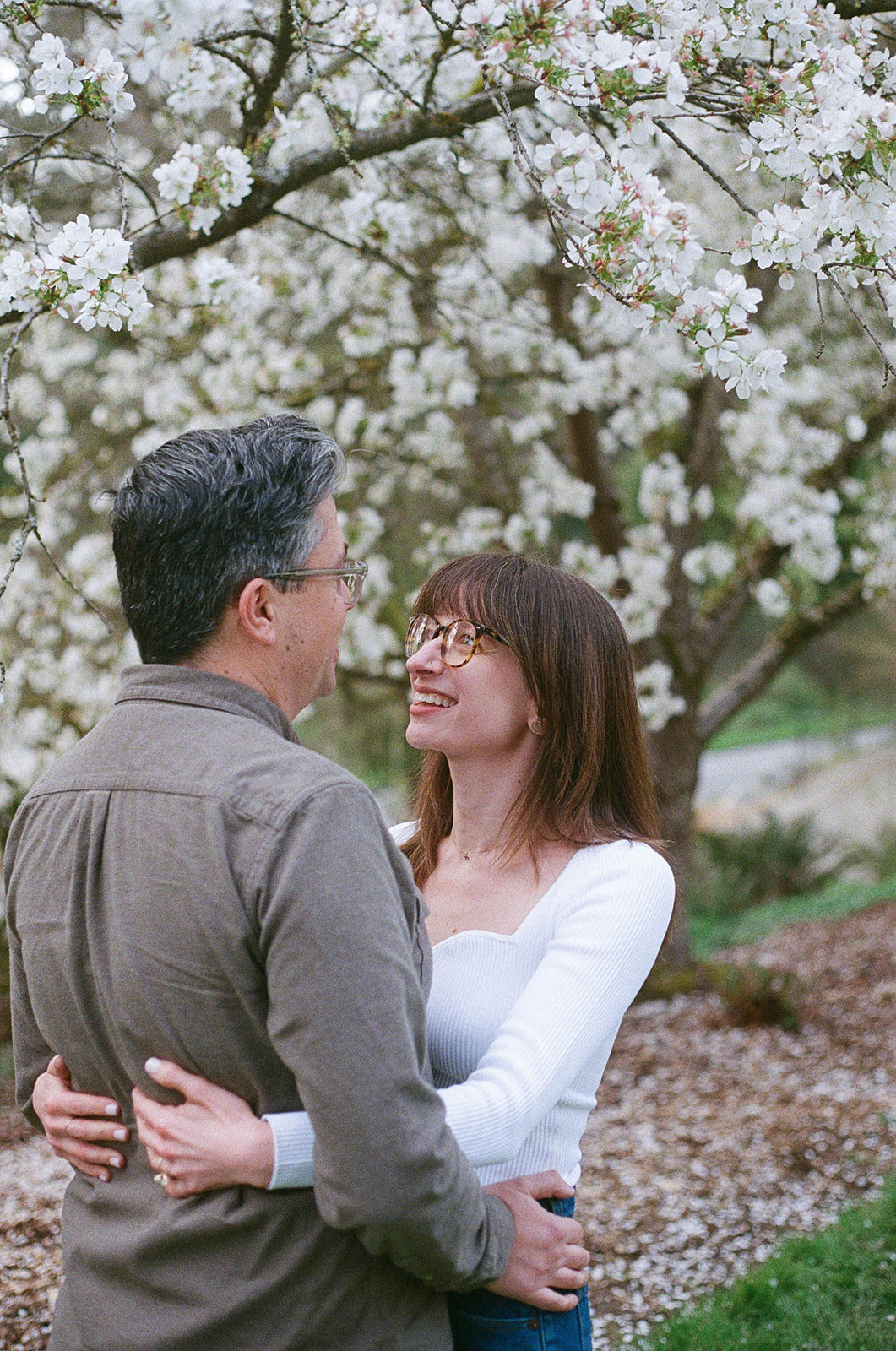 Charlotte and Grant embracing under a blooming cherry blossom tree, smiling at each other.