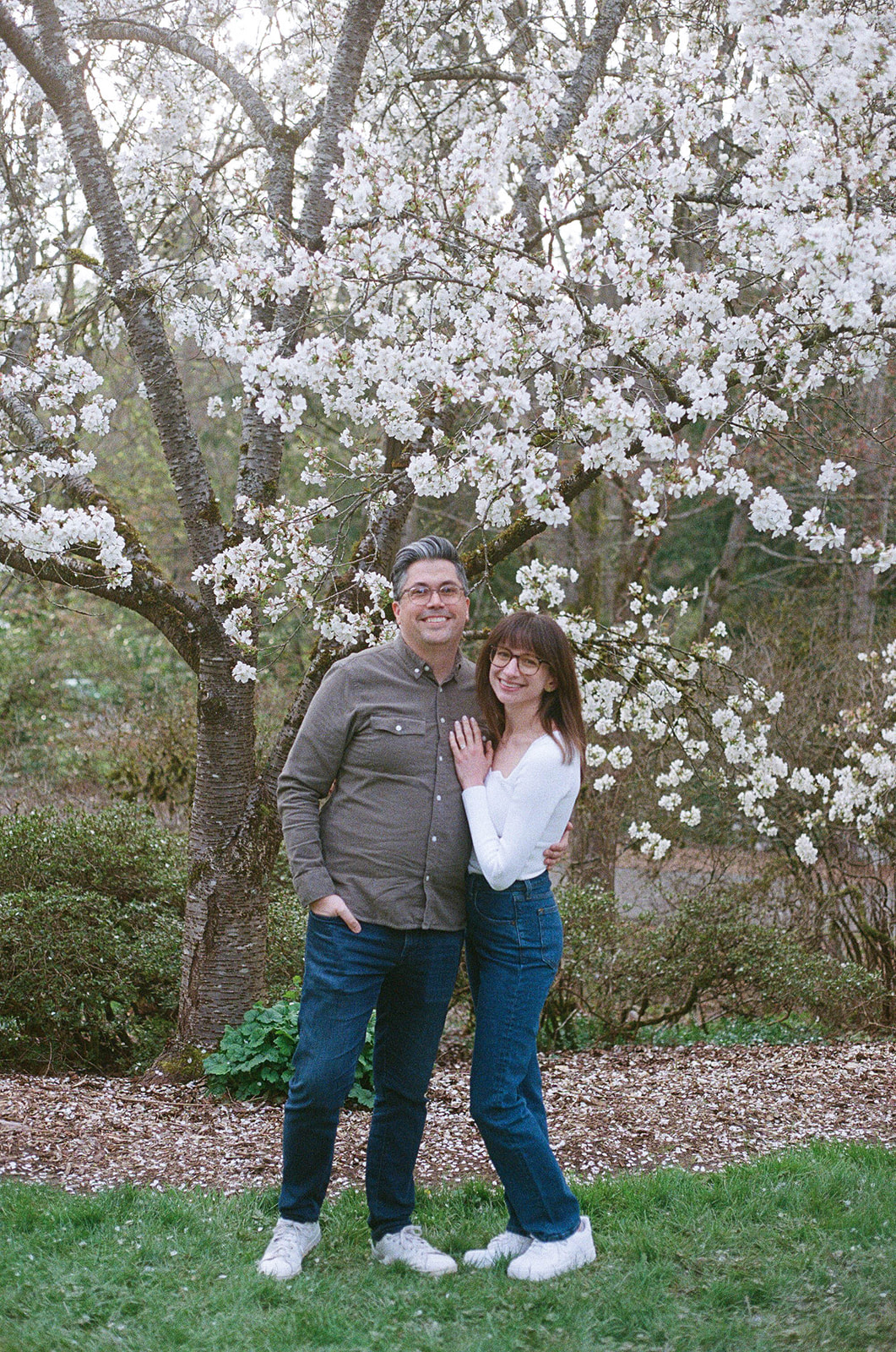 Charlotte and Grant standing in front of a blooming cherry blossom tree, smiling at the camera.