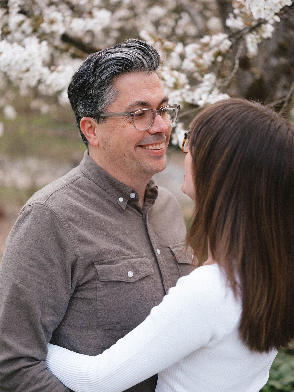 Close-up of Grant smiling while looking at Charlotte in front of blooming cherry blossoms.