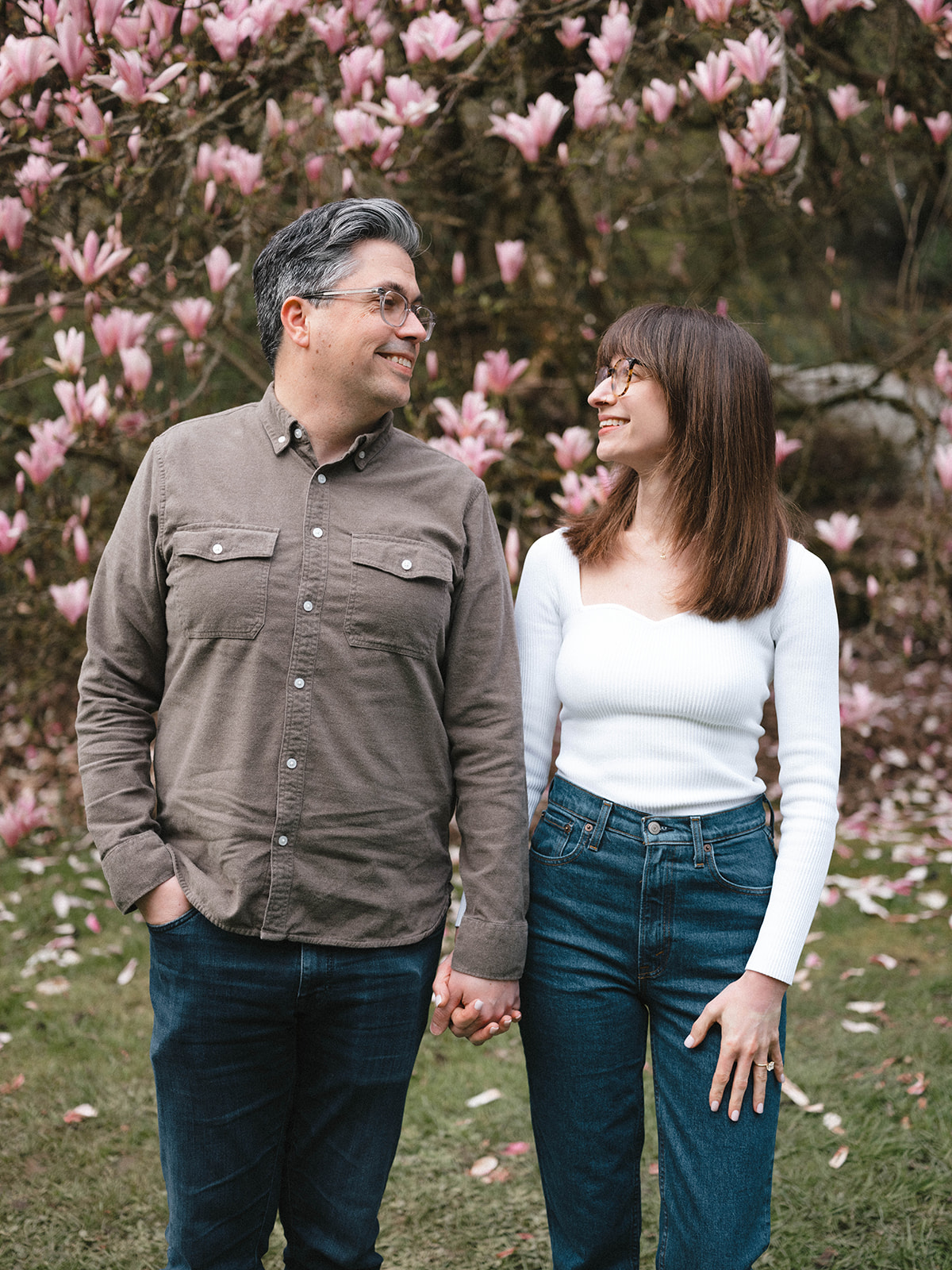 Charlotte and Grant standing in front of a magnolia tree in full bloom, holding hands and smiling at each other.