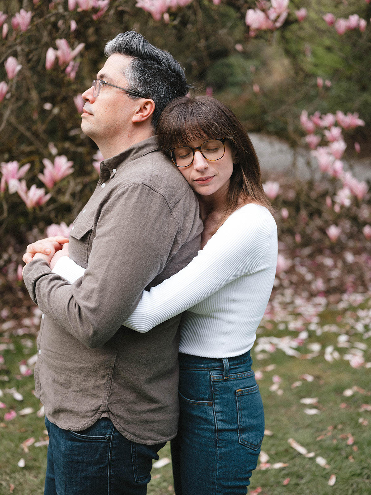 Charlotte hugging Grant from behind with closed eyes, in front of a blooming magnolia tree at the Washington Park Arboretum.