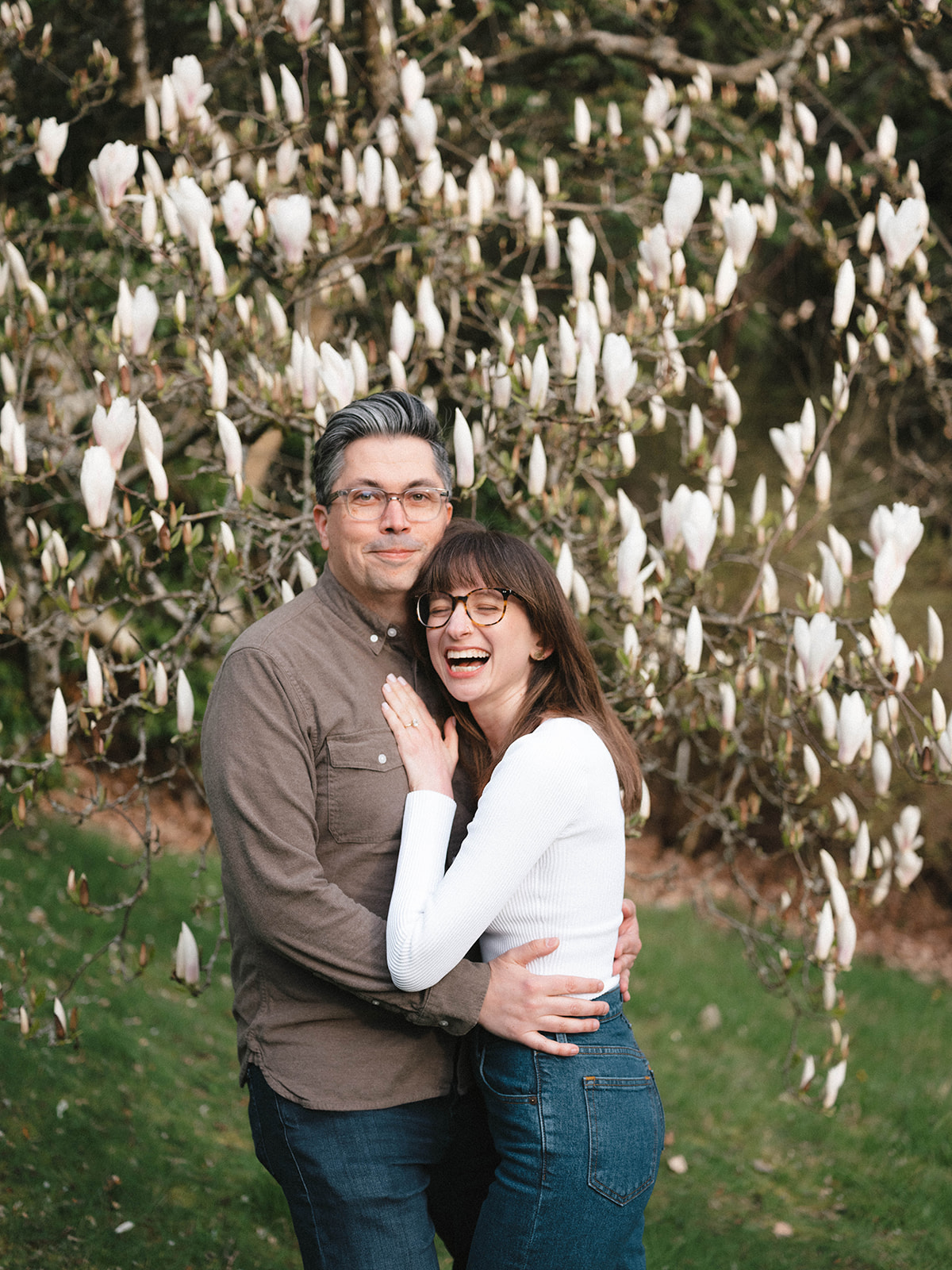 Couple smiling at each other with cherry blossoms in the background at Washington Park Arboretum.