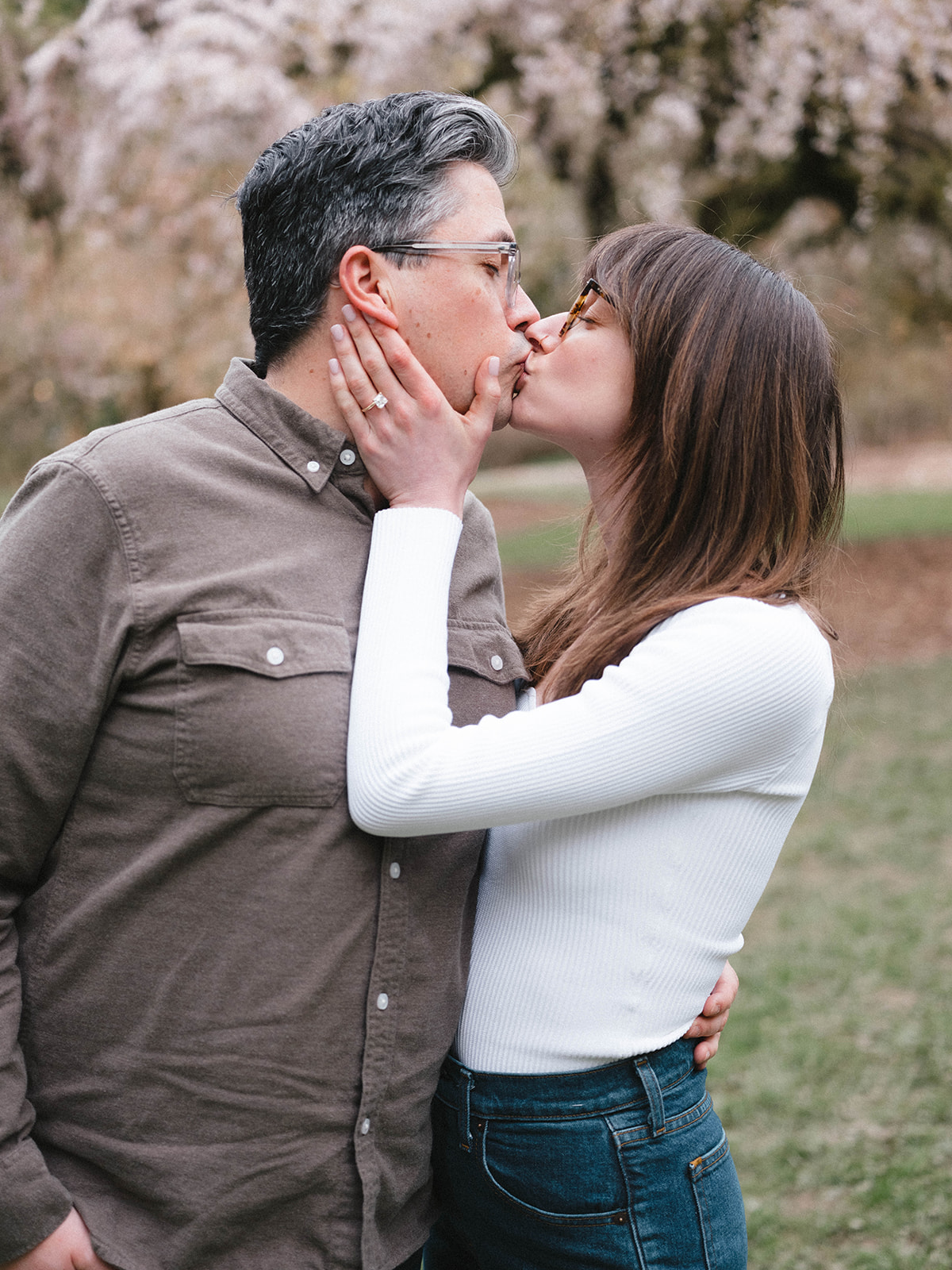 Couple sharing a kiss with cherry blossoms in the background.