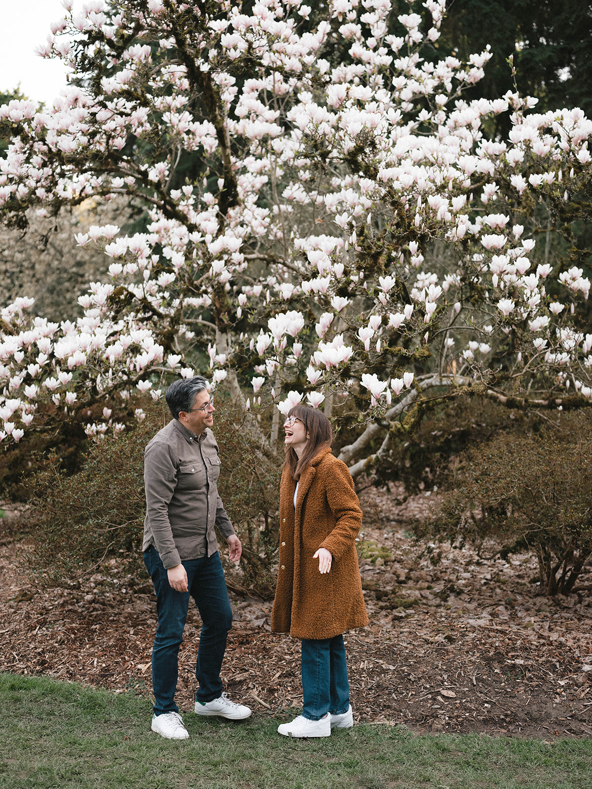 Charlotte and Grant laughing together under a blooming magnolia tree.