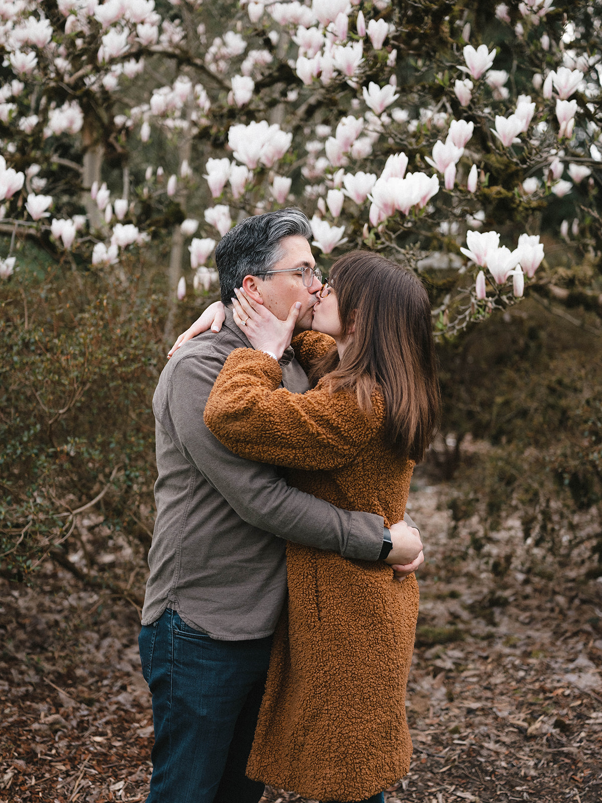 Charlotte and Grant kissing beneath a blooming magnolia tree.