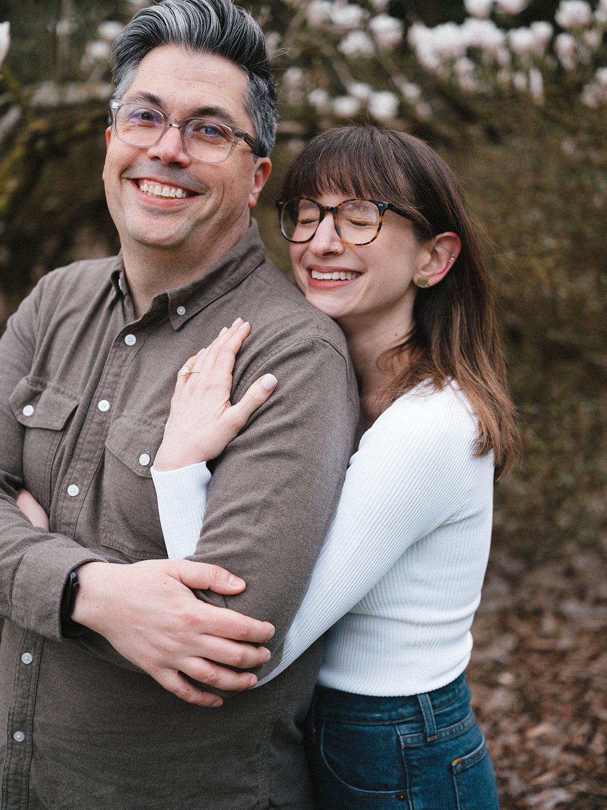 Charlotte resting her head on Grant’s back while they smile in front of blooming magnolia trees.