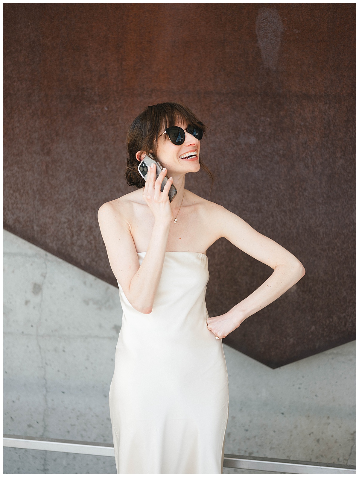 Charlotte laughing on the phone in a chic satin dress, sunglasses on, moments before her wedding.