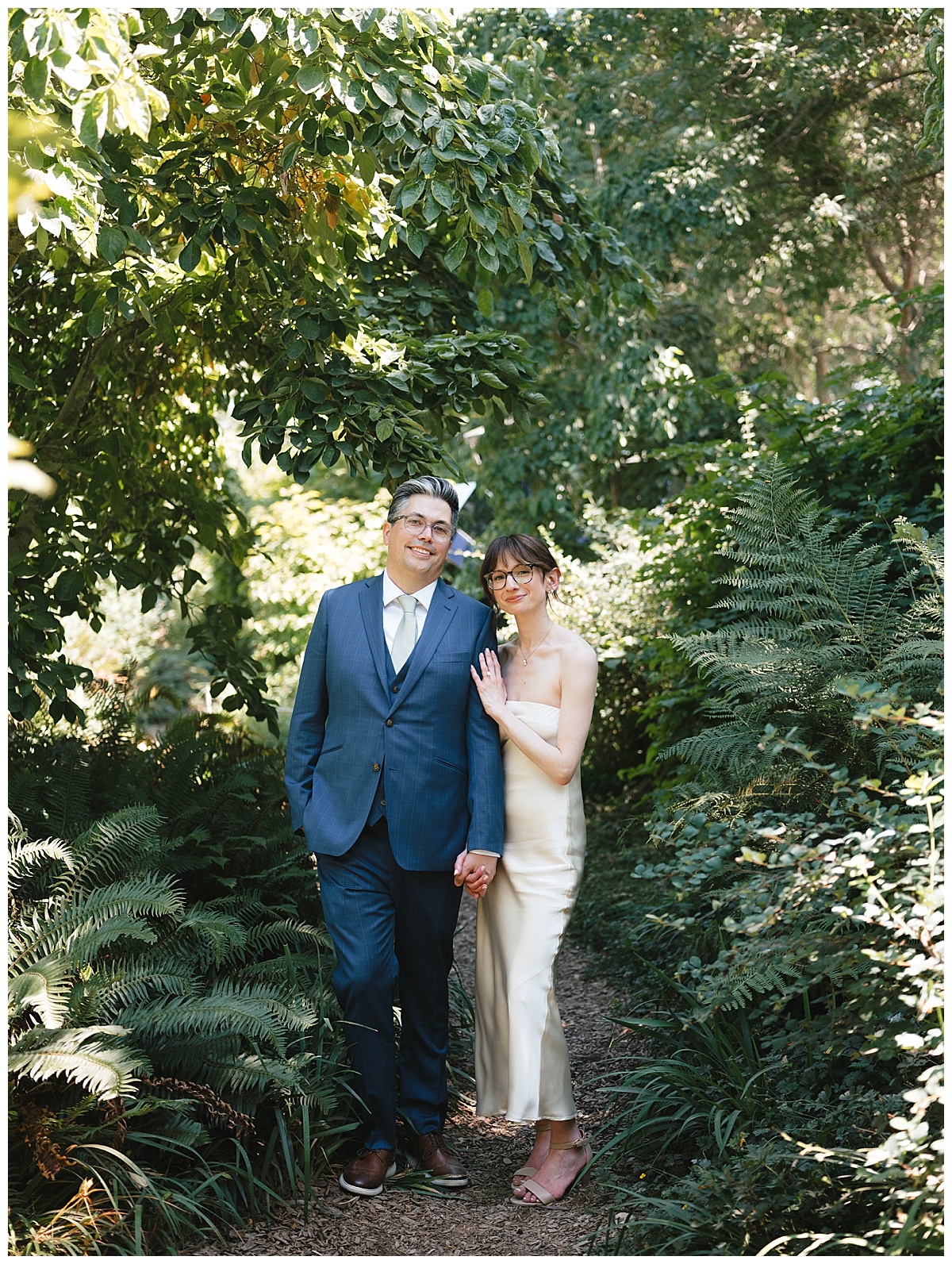 Groom lovingly kissing the bride on the head as they smile and embrace in front of a rust-colored sculpture.