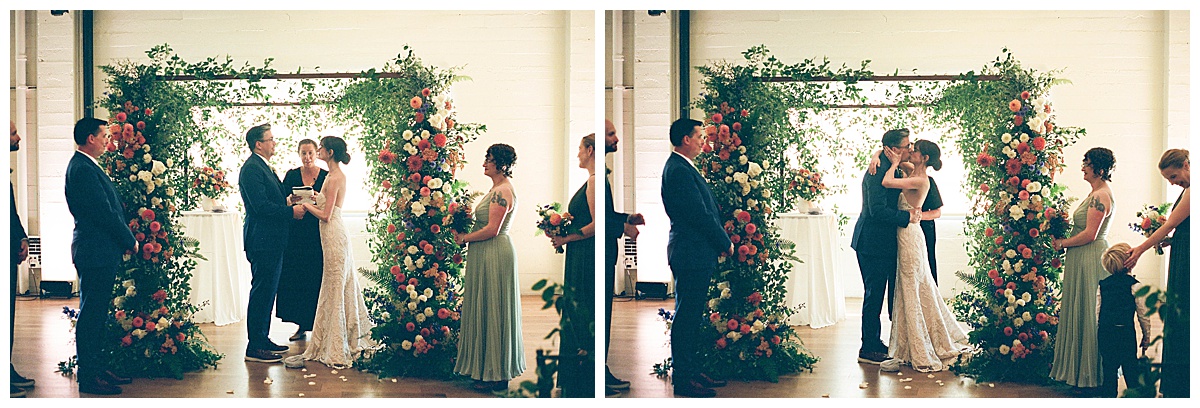 Bride and groom share a kiss under a floral arch at their Block41 wedding ceremony.