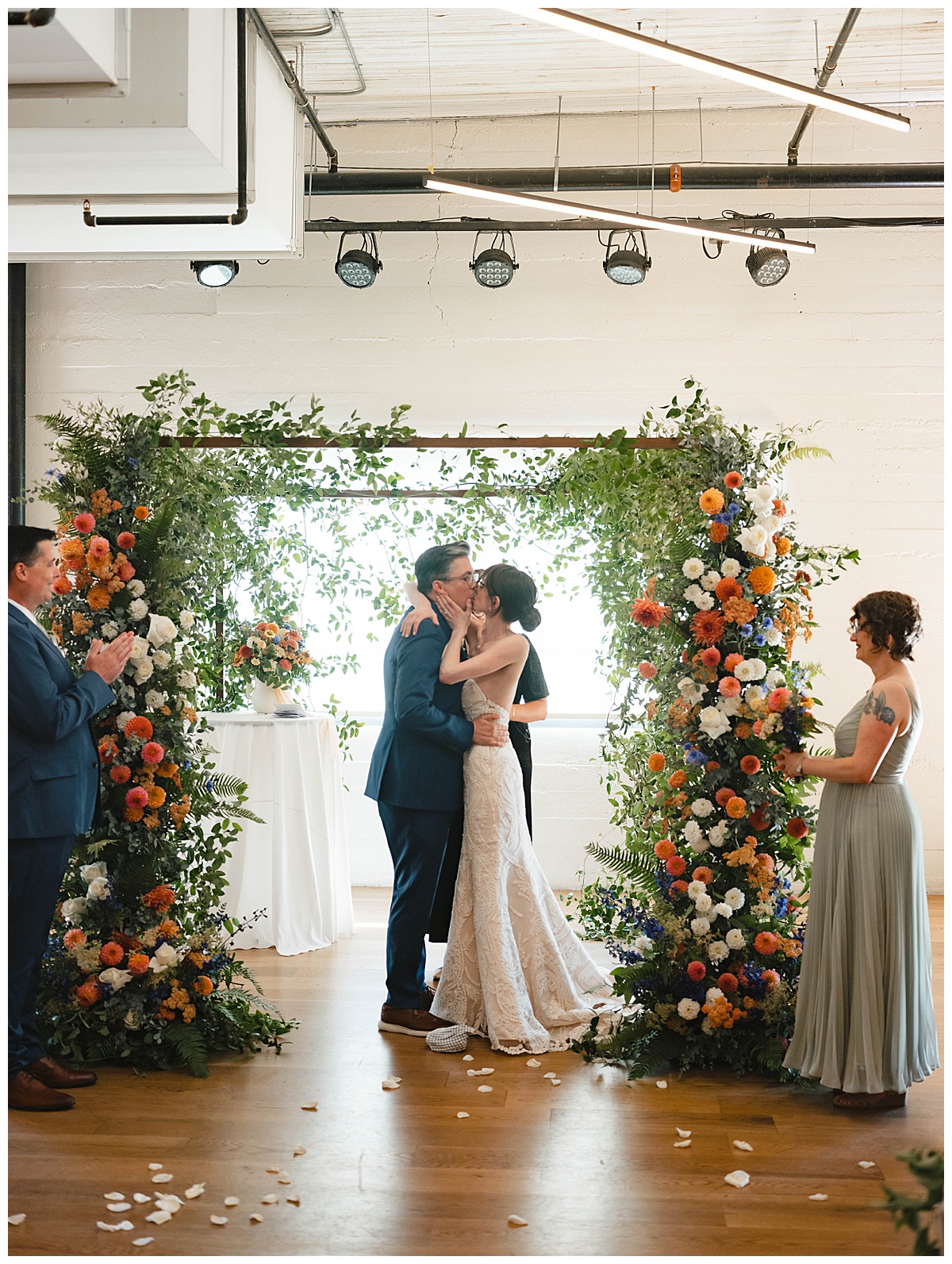 Bride and groom share their first kiss as a married couple under a floral arch.