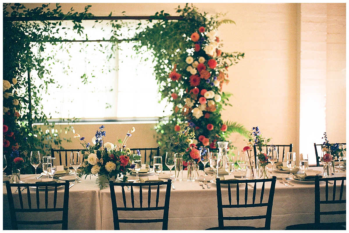 A beautifully decorated wedding reception table with lush floral arrangements in the background.