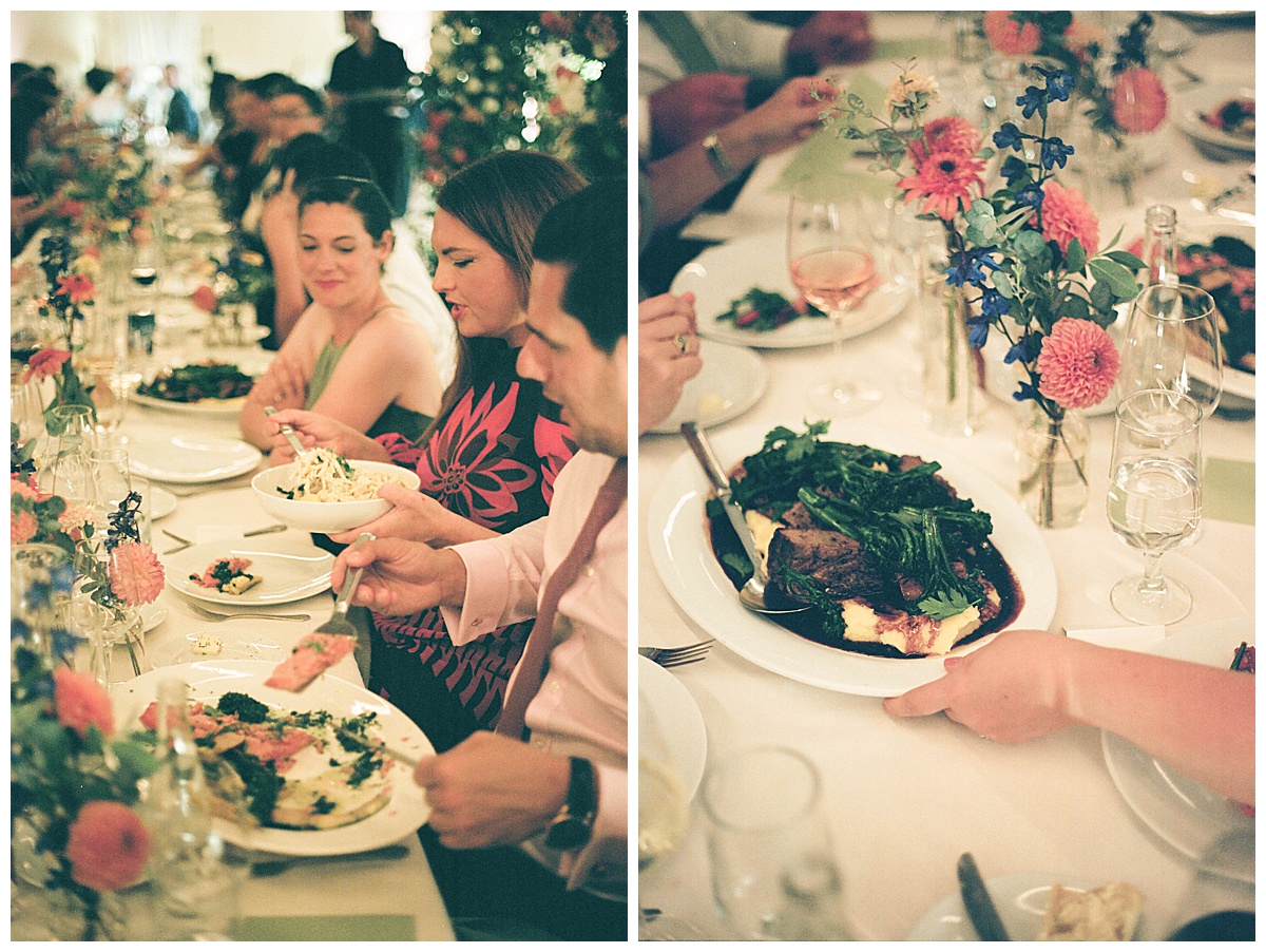 Guests enjoying their plated meals at a long banquet table decorated with flowers during the wedding reception.