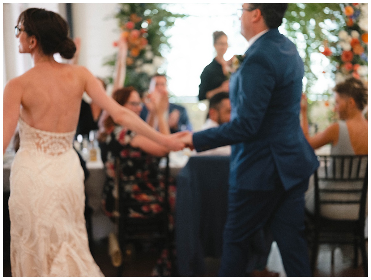 Bride and groom holding hands as they walk together through the reception, smiling and celebrating with guests.