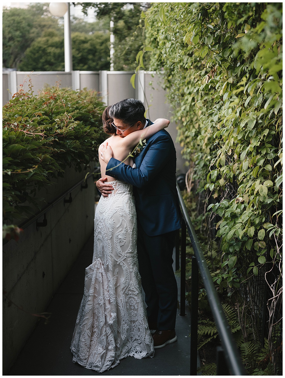 The bride and groom embrace in a quiet moment, surrounded by lush greenery.