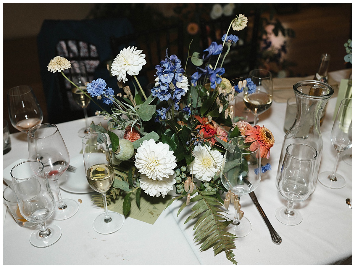 A colorful floral centerpiece with wine glasses on a table after a reception meal.