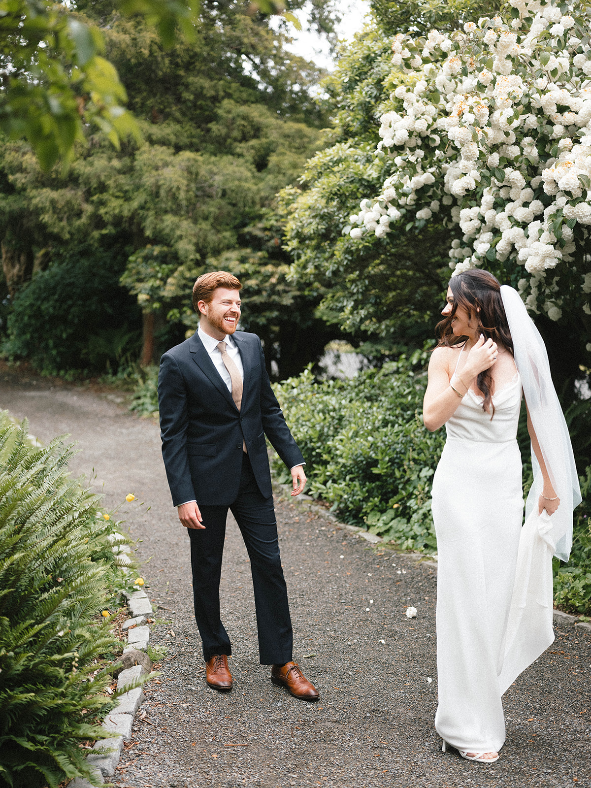 Groom smiling and laughing as the bride spins around during their first look in a lush garden at Parsons Gardens.