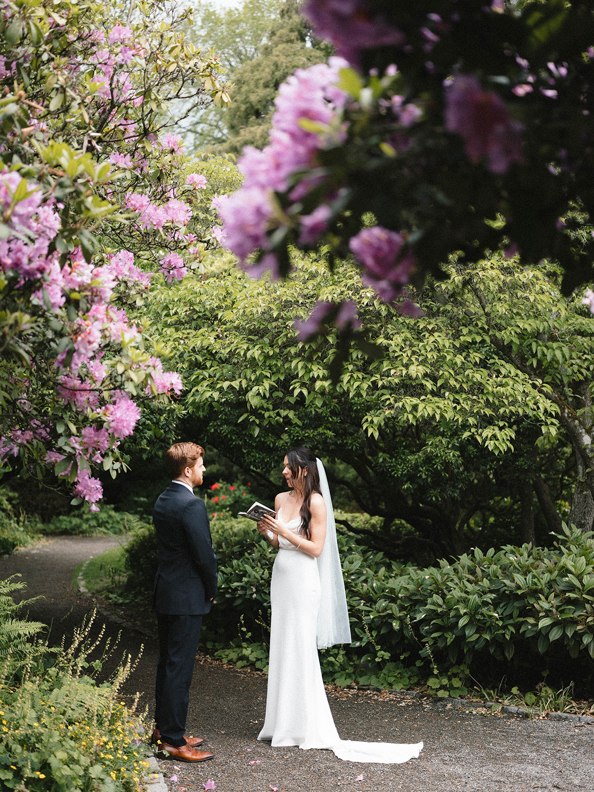 Bride reading her vows to the groom while standing under blooming pink flowers at Parsons Gardens.